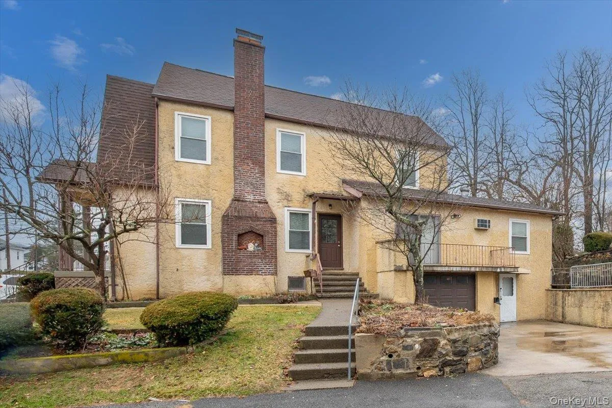 View of side of home featuring stucco siding, a chimney, an attached garage, and driveway View of side of home featuring stucco siding, a chimney, an attached garage, and driveway