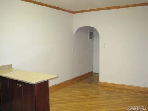 Empty room featuring ornamental molding, arched walkways, and light wood finished floors Empty room featuring ornamental molding, arched walkways, and light wood finished floors