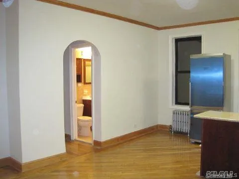 Spare room featuring crown molding, radiator heating unit, arched walkways, and light wood-type flooring Spare room featuring crown molding, radiator heating unit, arched walkways, and light wood-type flooring