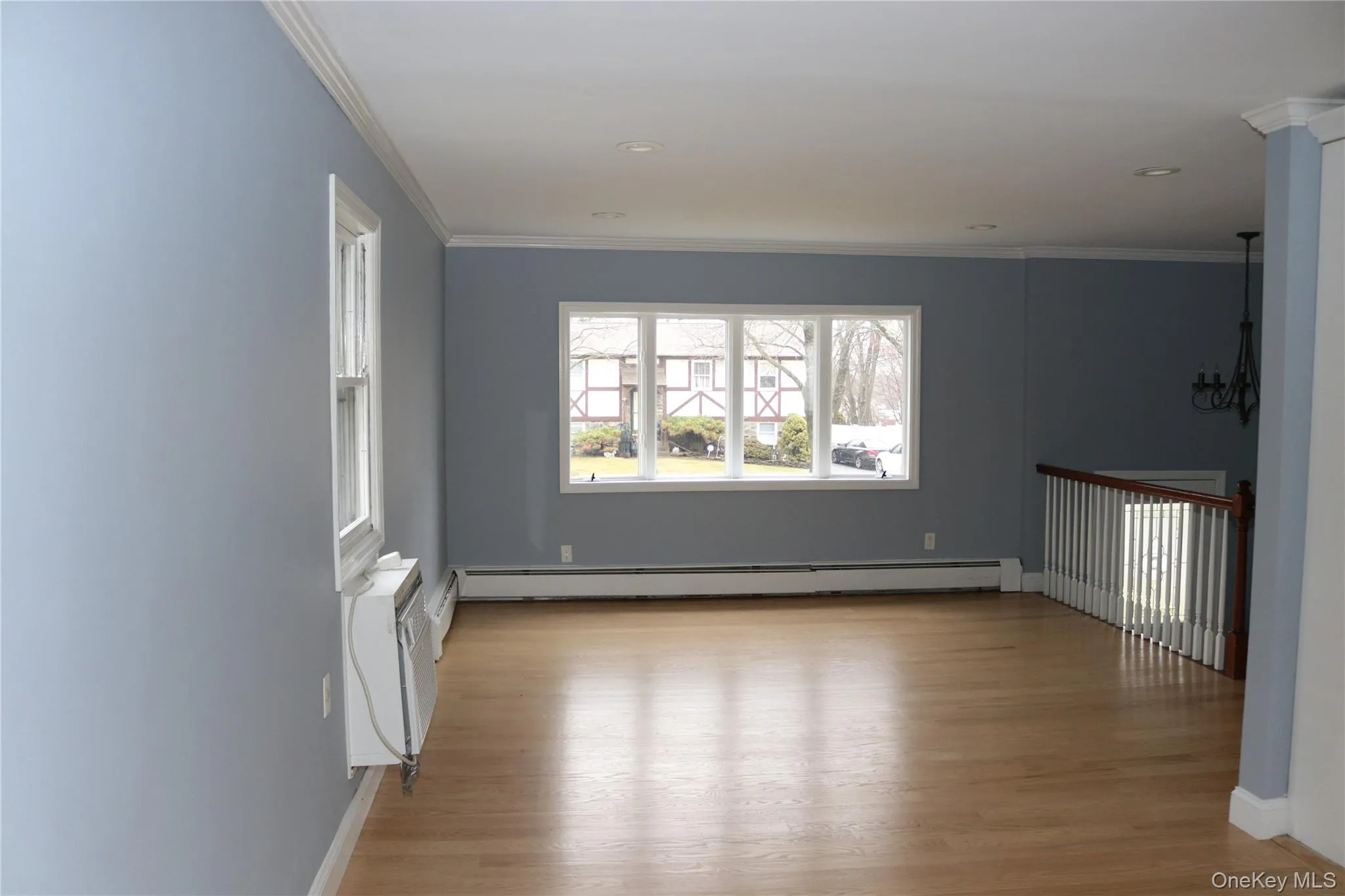 Living room with dining room space featuring light wood finished floors, crown molding, baseboard heating, and hanging lights Living room with dining room space featuring light wood finished floors, crown molding, baseboard heating, and hanging lights