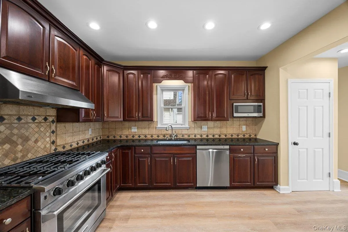 Kitchen with stainless steel appliances, light wood finished floors, dark stone countertops, dark wood finish cabinets, and recessed lighting Kitchen with stainless steel appliances, light wood finished floors, dark stone countertops, dark wood finish cabinets, and recessed lighting