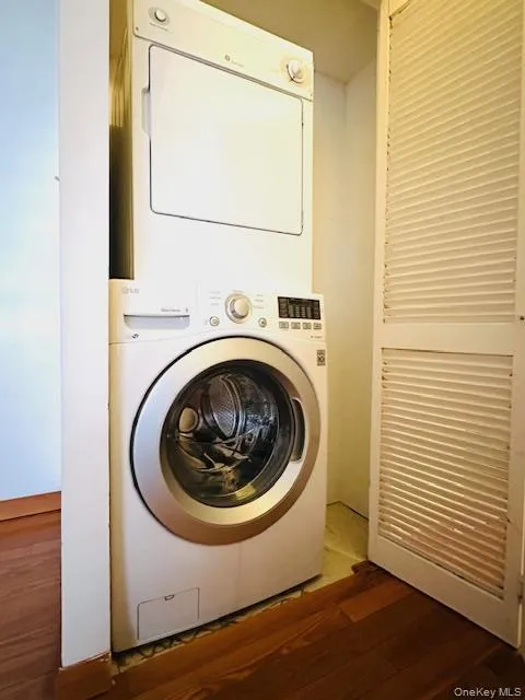 Laundry area featuring dark wood finished floors and stacked washing machine and dryer Laundry area featuring dark wood finished floors and stacked washing machine and dryer