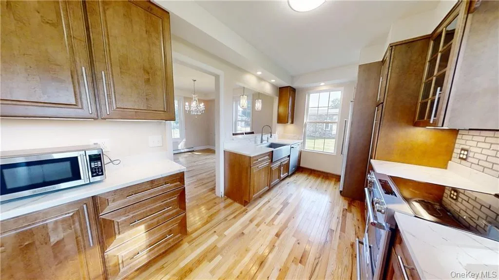 Kitchen featuring glass insert cabinets, appliances with stainless steel finishes, light wood-style floors, brown cabinets, and a chandelier Kitchen featuring glass insert cabinets, appliances with stainless steel finishes, light wood-style floors, brown cabinets, and a chandelier