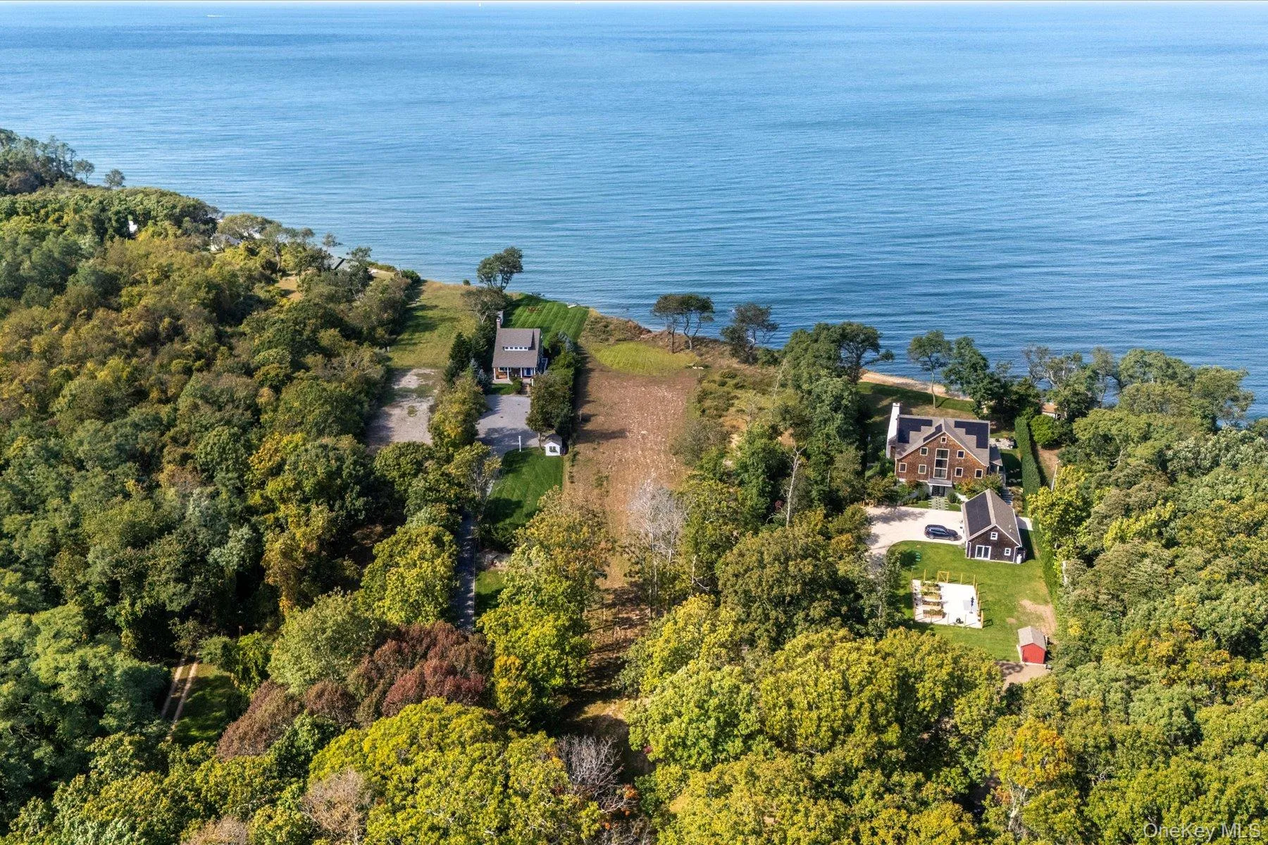Aerial view highlighting the property's prime position near the waterfront, surrounded by mature trees and neighboring residencees, with the shoreline and open water just beyond. Aerial view highlighting the property's prime position near the waterfront, surrounded by mature trees and neighboring residencees, with the shoreline and open water just beyond.