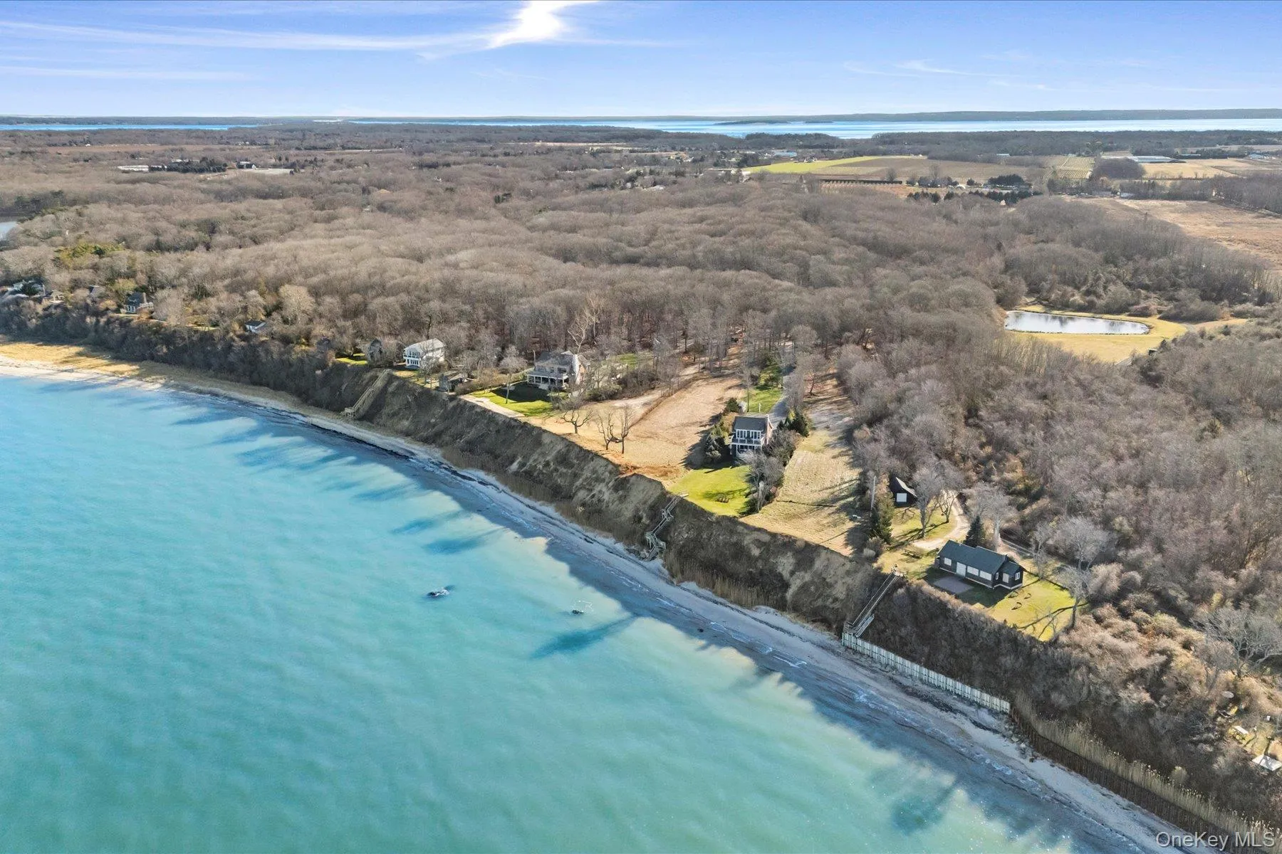 Elevated aerial showcasing a dramatic waterfront land parcel along the bluff, with expansive shoreline views, neighboring properties, and miles of scenic North Fork landscape stretching into the distance. Elevated aerial showcasing a dramatic waterfront land parcel along the bluff, with expansive shoreline views, neighboring properties, and miles of scenic North Fork landscape stretching into the distance.