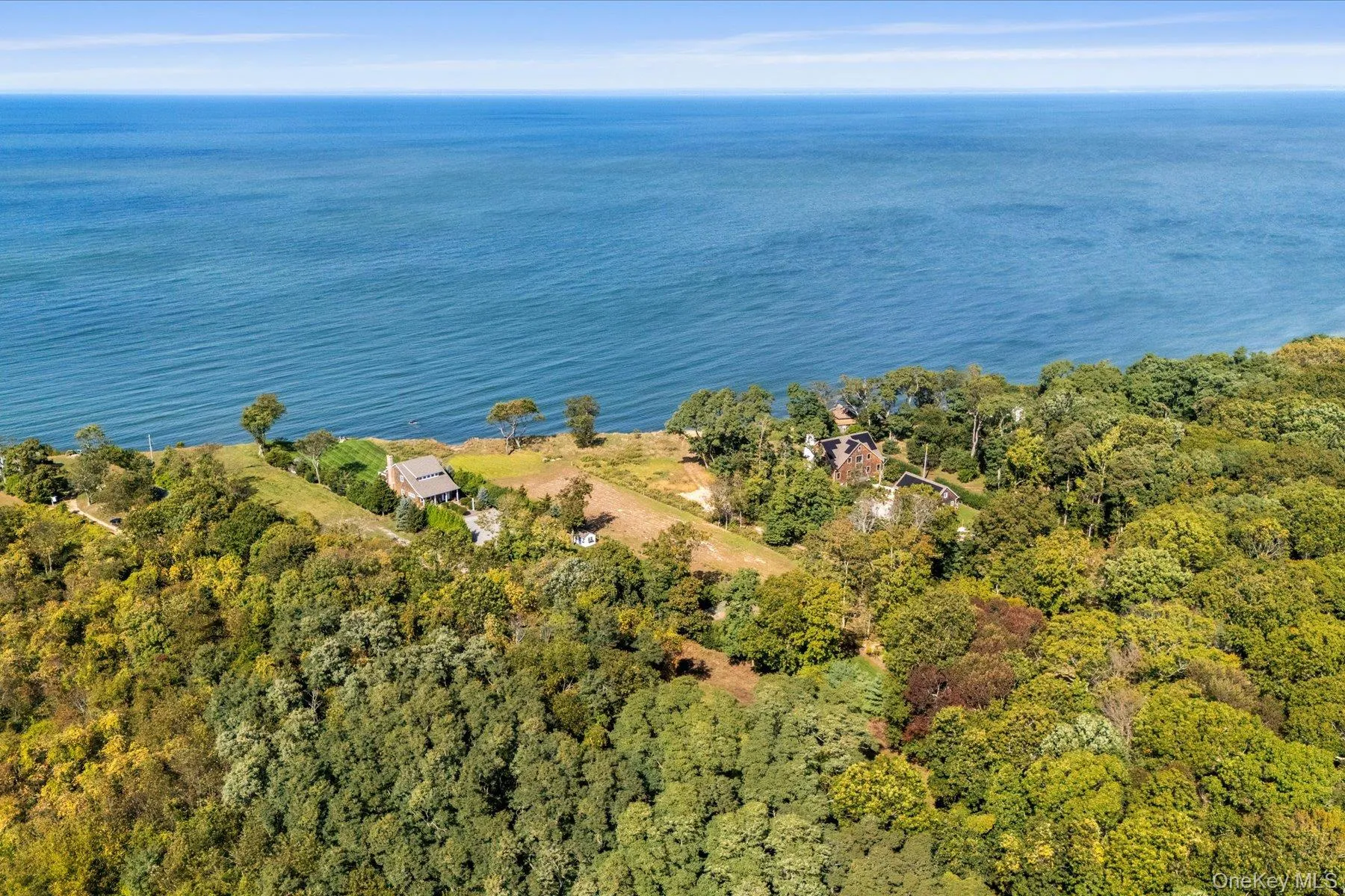 High aerial view showcasing the property's exceptional proximity to the waterfront, surrounded by mature trees and neighboring properties, with expansive open-water views beyond. High aerial view showcasing the property's exceptional proximity to the waterfront, surrounded by mature trees and neighboring properties, with expansive open-water views beyond.