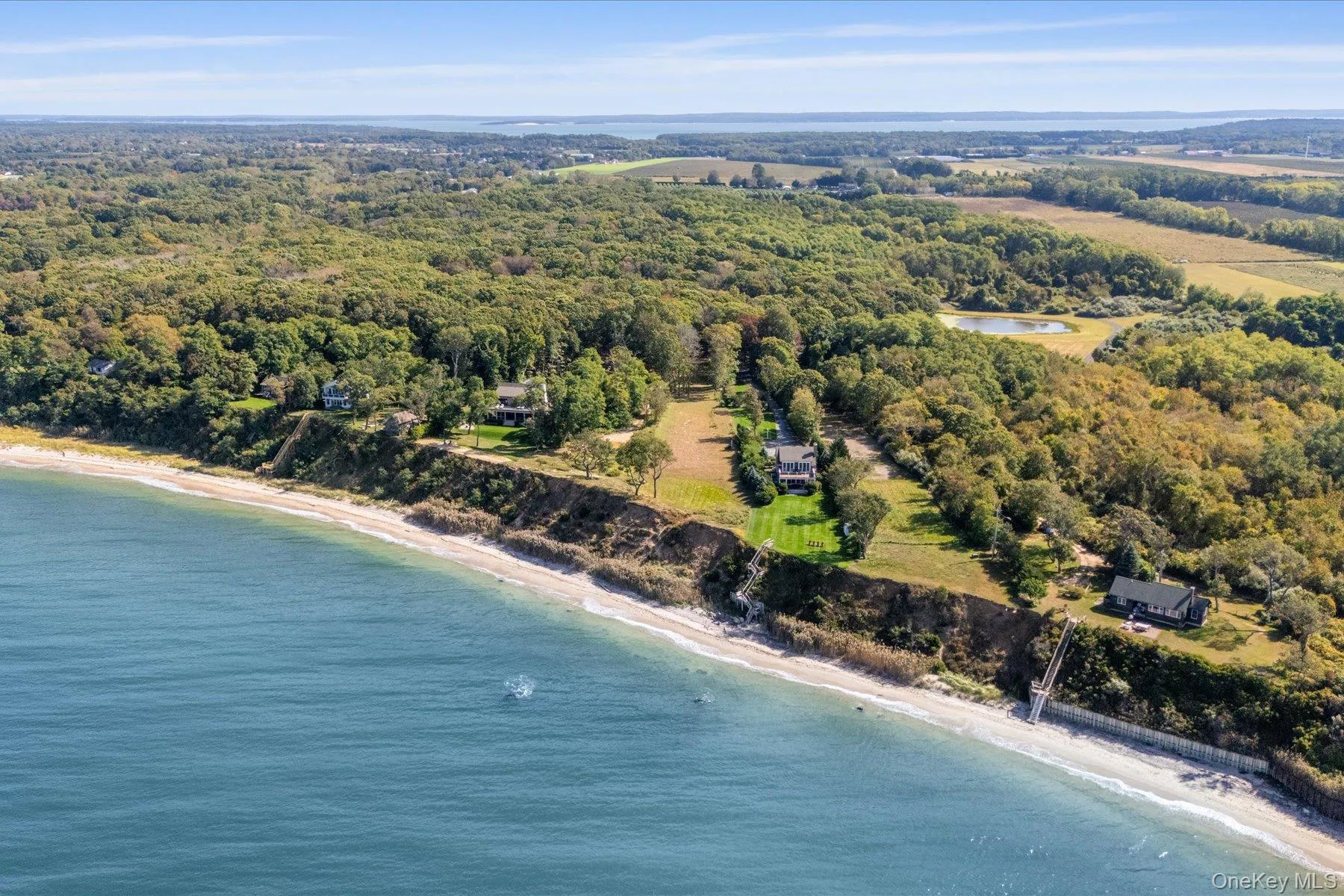 Wide aerial perspective of the North Fork shoreline, showcasing the property's waterfront setting along the bluff, neighboring homes, and expansive open land with Sound views stretching into the distance Wide aerial perspective of the North Fork shoreline, showcasing the property's waterfront setting along the bluff, neighboring homes, and expansive open land with Sound views stretching into the distance