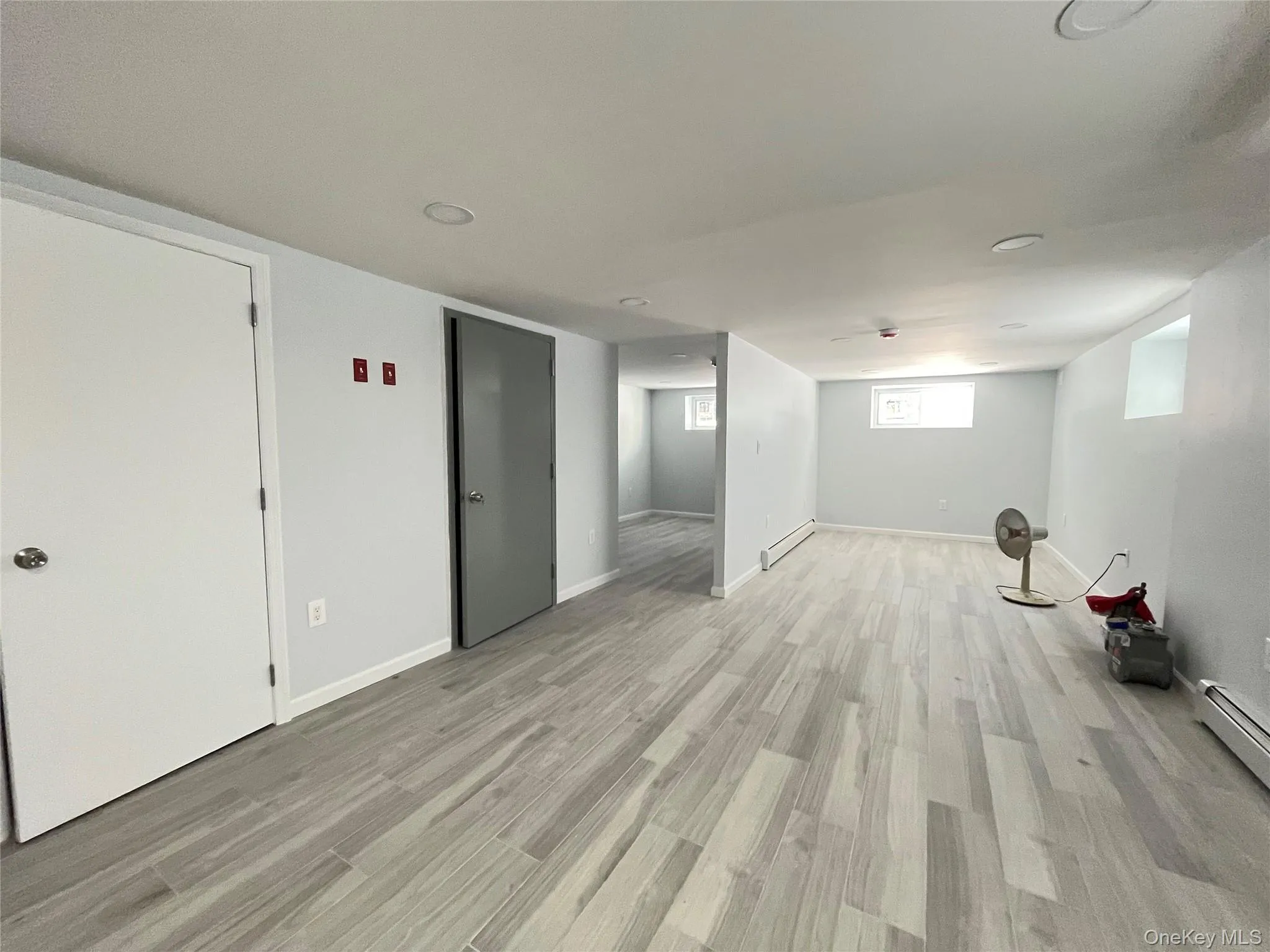 Below grade area featuring light wood finished floors and a baseboard heating unit Below grade area featuring light wood finished floors and a baseboard heating unit