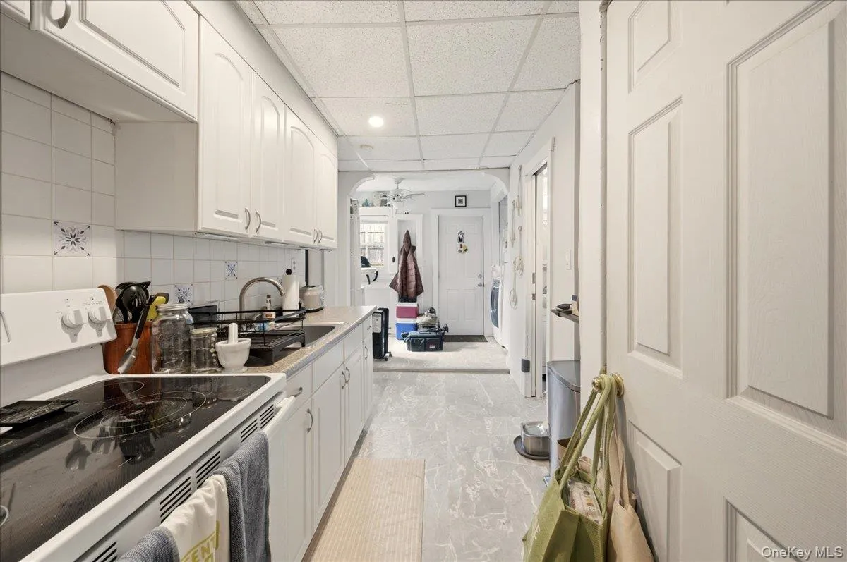 Kitchen featuring white range with electric cooktop, white cabinets, a drop ceiling, decorative backsplash, and arched walkways Kitchen featuring white range with electric cooktop, white cabinets, a drop ceiling, decorative backsplash, and arched walkways