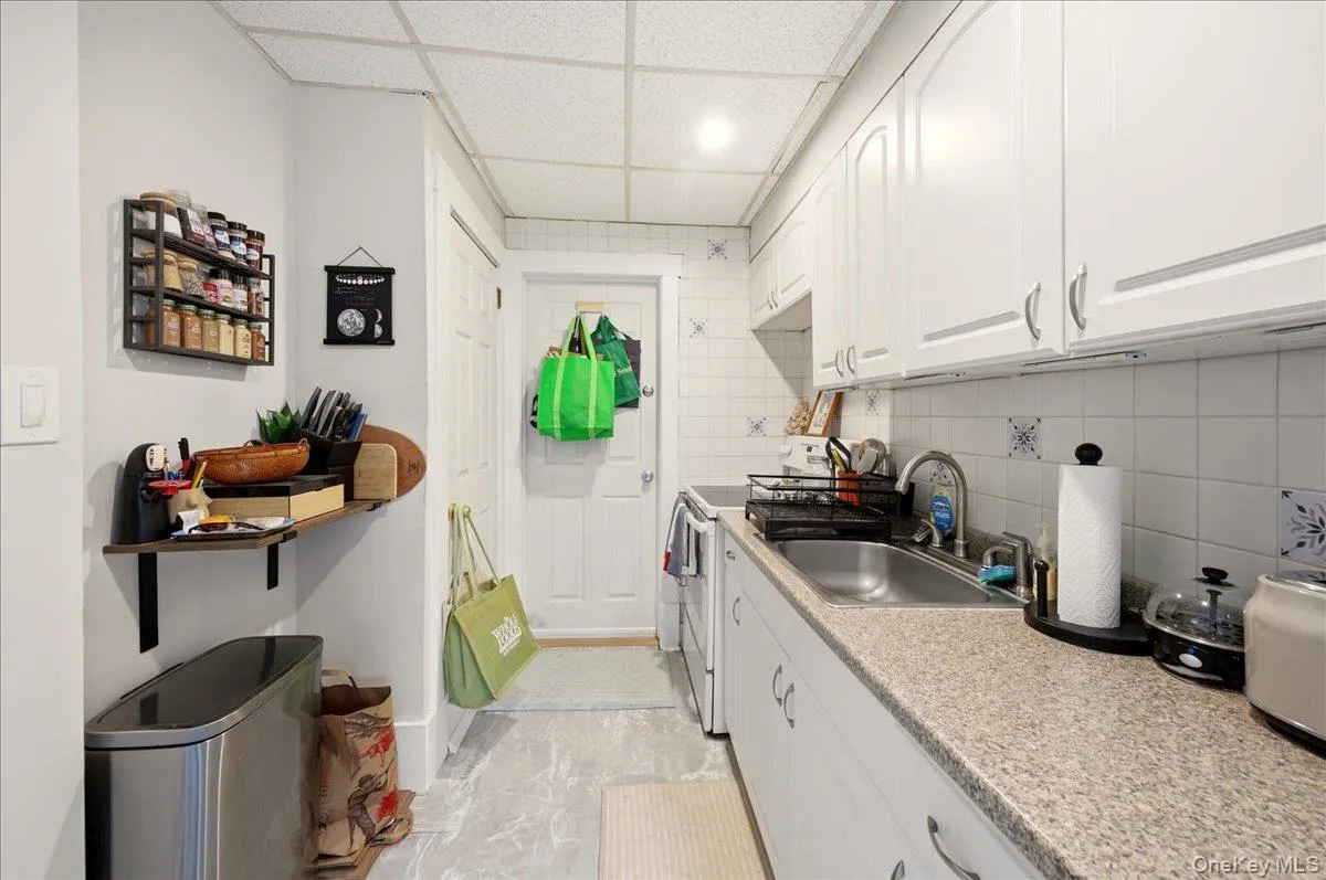 Kitchen with white cabinets, a drop ceiling, tasteful backsplash, and electric stove Kitchen with white cabinets, a drop ceiling, tasteful backsplash, and electric stove