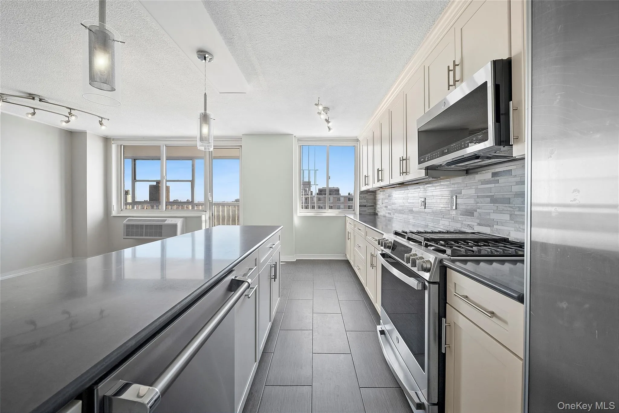 Kitchen with stainless steel appliances, dark stone countertops, pendant lighting, decorative backsplash, and a textured ceiling Kitchen with stainless steel appliances, dark stone countertops, pendant lighting, decorative backsplash, and a textured ceiling
