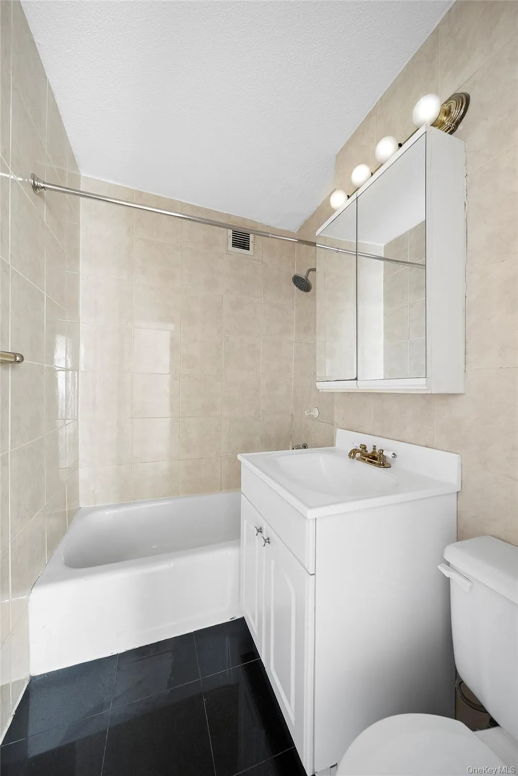 Bathroom with vanity, bathing tub / shower combination, tile walls, and dark tile patterned flooring Bathroom with vanity, bathing tub / shower combination, tile walls, and dark tile patterned flooring