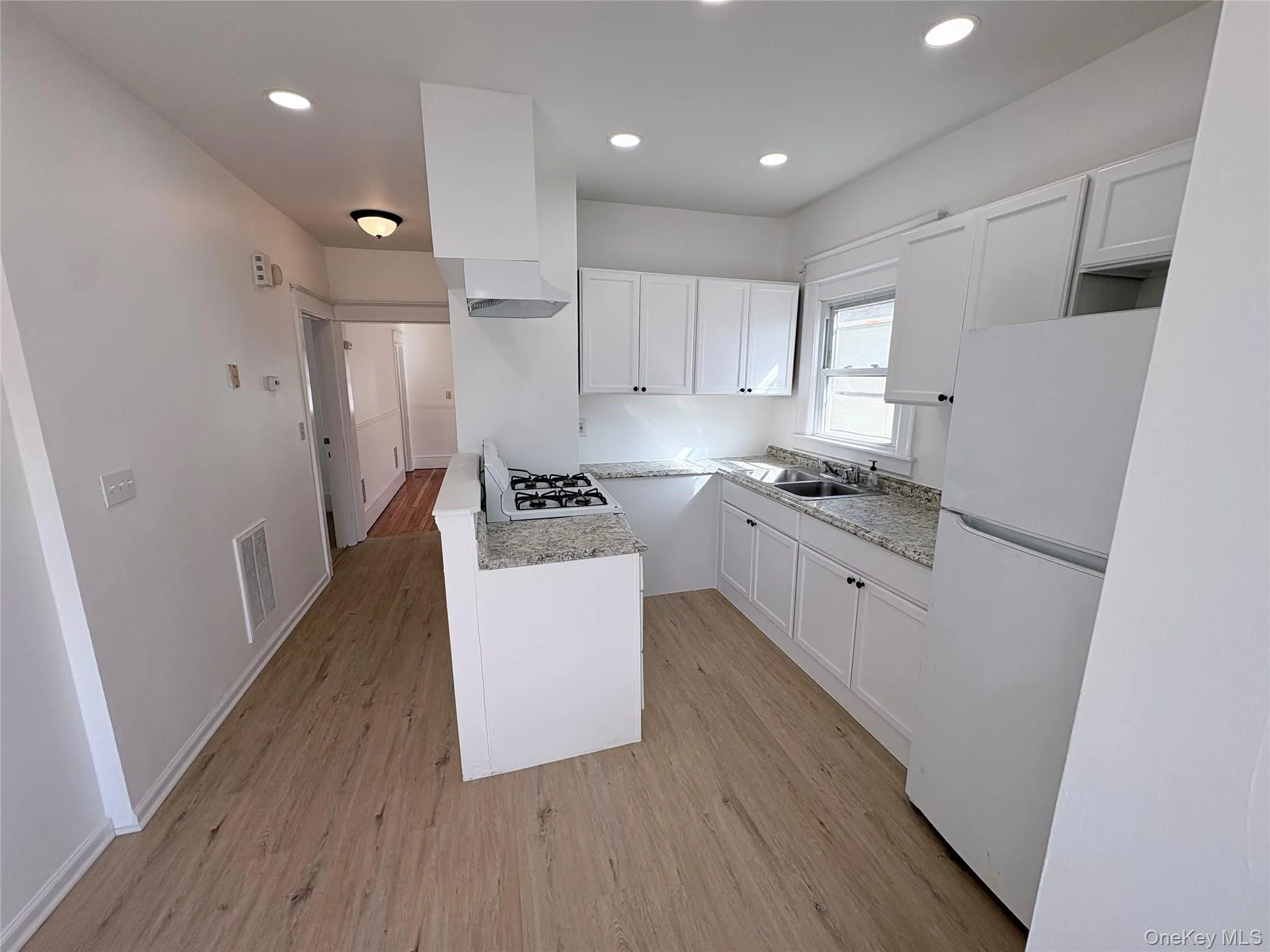 Kitchen with white appliances, white cabinets, light wood-style flooring, and recessed lighting Kitchen with white appliances, white cabinets, light wood-style flooring, and recessed lighting