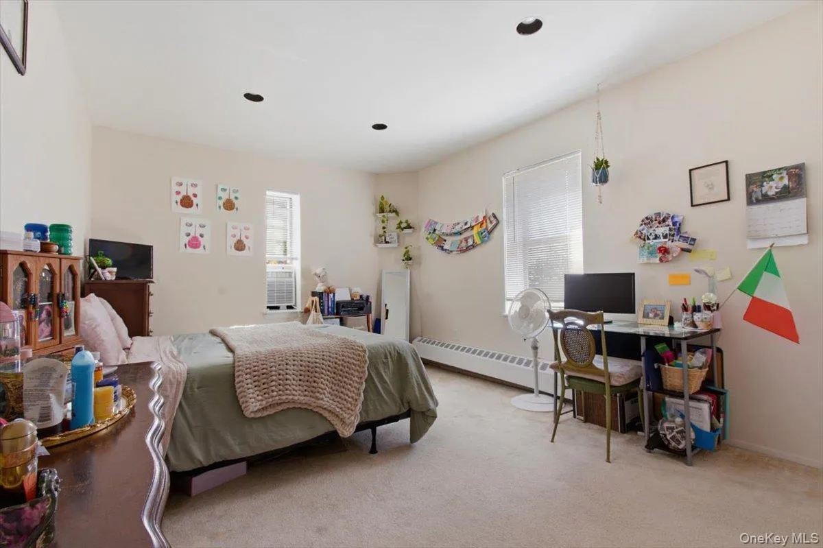 Bedroom featuring light colored carpet, baseboard heating, and a desk Bedroom featuring light colored carpet, baseboard heating, and a desk