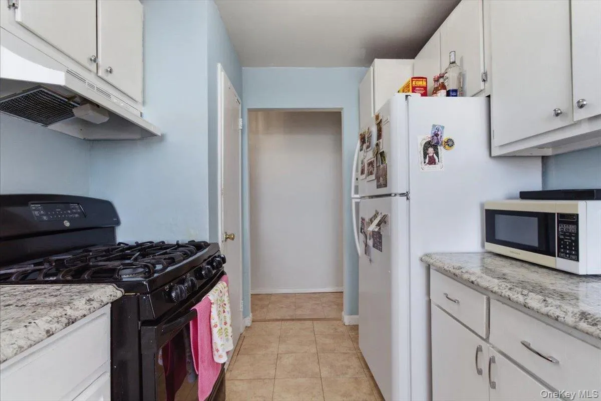 Kitchen with black gas stove, white cabinets, light stone counters, light tile patterned floors, and freestanding refrigerator Kitchen with black gas stove, white cabinets, light stone counters, light tile patterned floors, and freestanding refrigerator