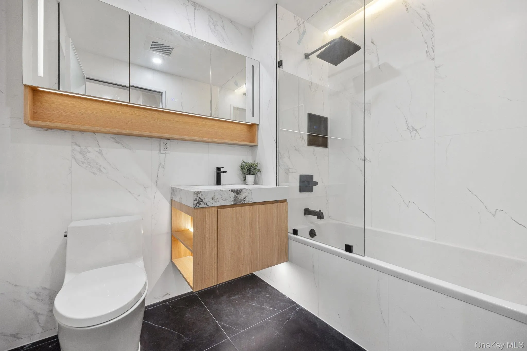 Bathroom featuring marble tiled flooring, toilet, a combined bath / shower with marble appearance, and vanity Bathroom featuring marble tiled flooring, toilet, a combined bath / shower with marble appearance, and vanity