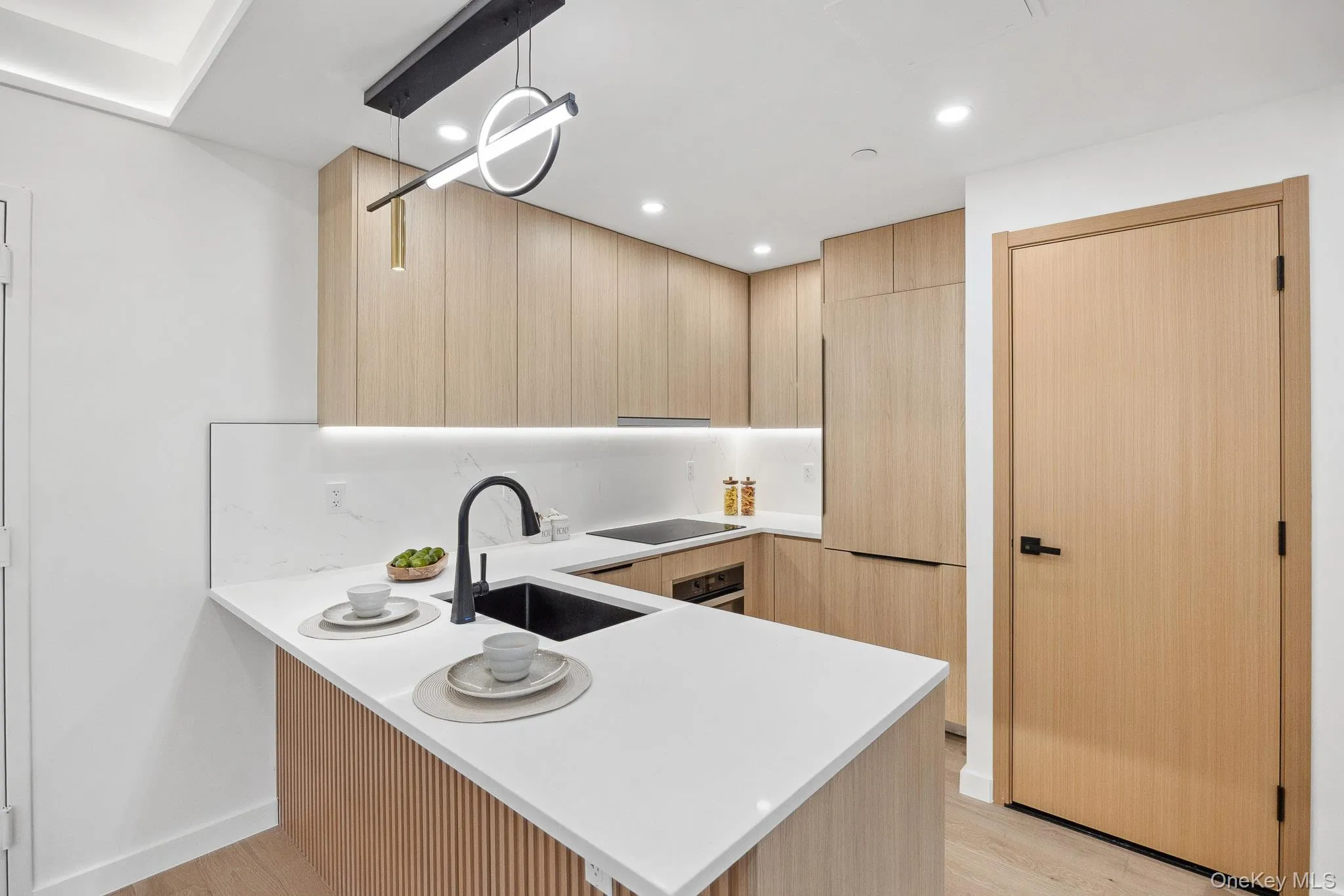 Kitchen with light brown cabinetry, a sink, light countertops, a peninsula, and light wood-style flooring Kitchen with light brown cabinetry, a sink, light countertops, a peninsula, and light wood-style flooring