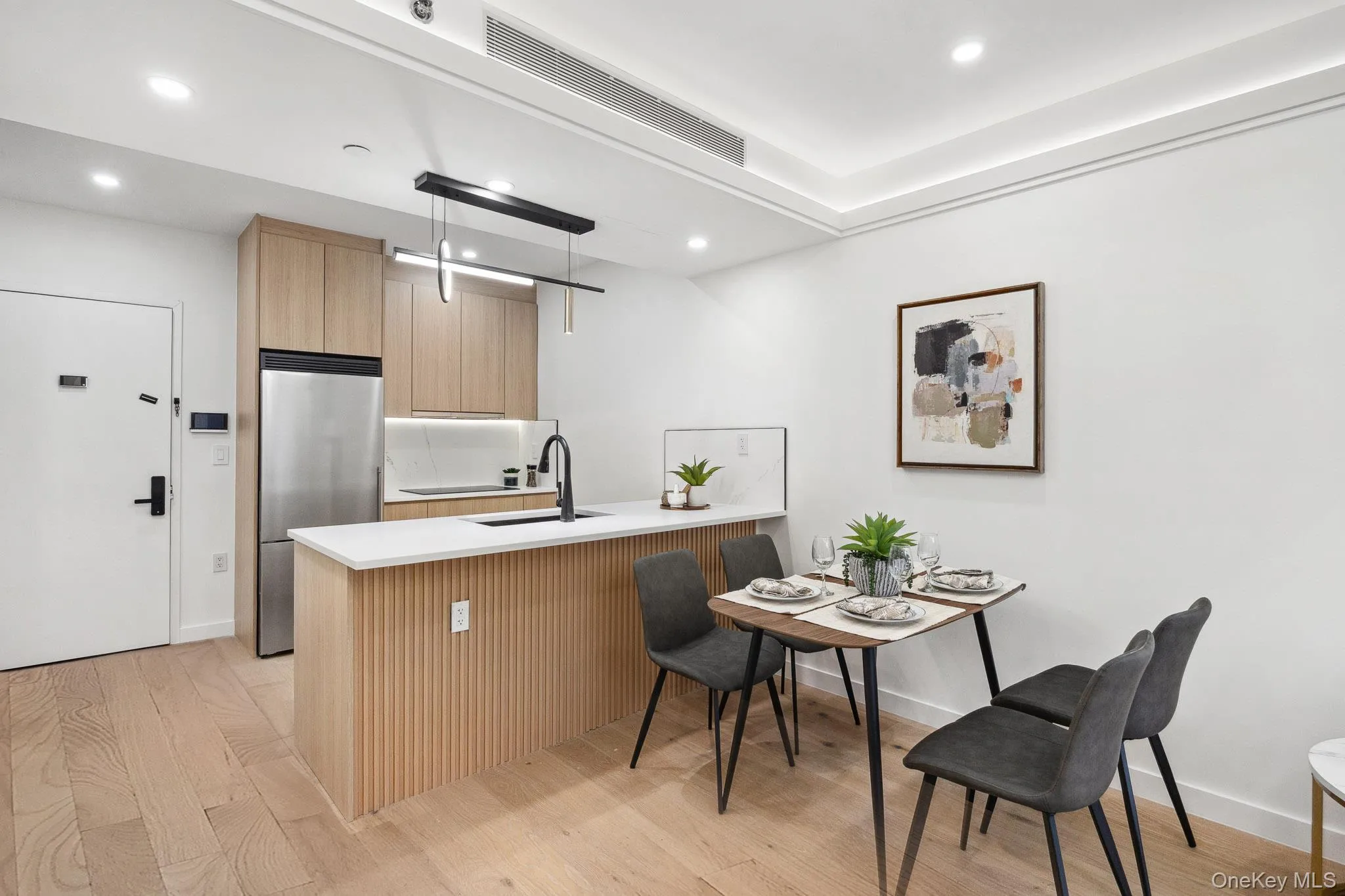 Kitchen featuring stainless steel refrigerator, a sink, light brown cabinetry, a peninsula, and light wood-type flooring Kitchen featuring stainless steel refrigerator, a sink, light brown cabinetry, a peninsula, and light wood-type flooring