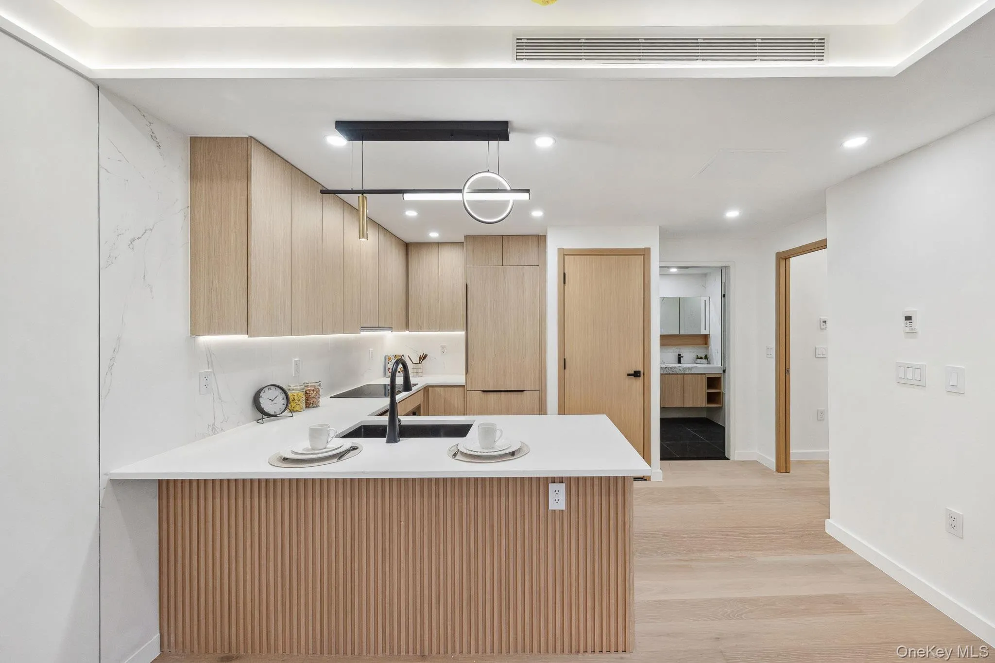 Kitchen featuring light brown cabinets, a peninsula, a sink, light wood-type flooring, and light countertops Kitchen featuring light brown cabinets, a peninsula, a sink, light wood-type flooring, and light countertops