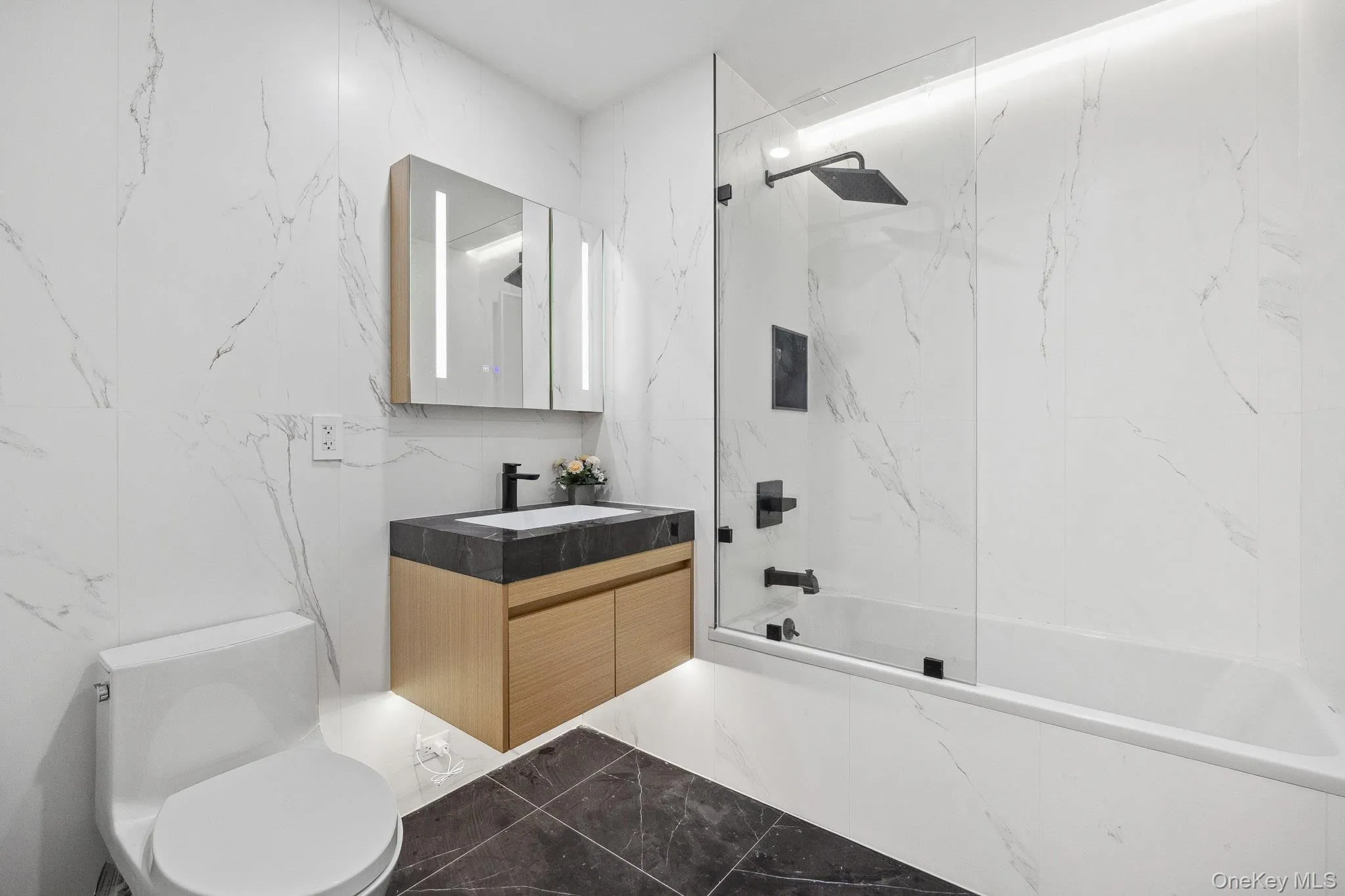 Bathroom with marble tiled floors, vanity, bathtub / shower combination, and toilet Bathroom with marble tiled floors, vanity, bathtub / shower combination, and toilet