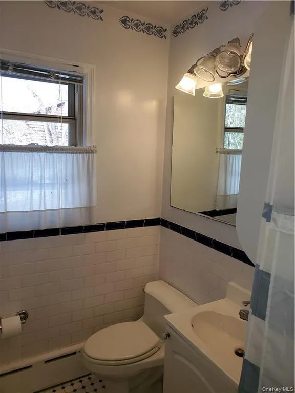 Bathroom with toilet, tile patterned floors, tile walls, and a healthy amount of sunlight Bathroom with toilet, tile patterned floors, tile walls, and a healthy amount of sunlight