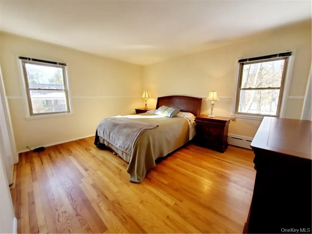 Bedroom featuring light wood-style floors, multiple windows, and a baseboard heating unit Bedroom featuring light wood-style floors, multiple windows, and a baseboard heating unit