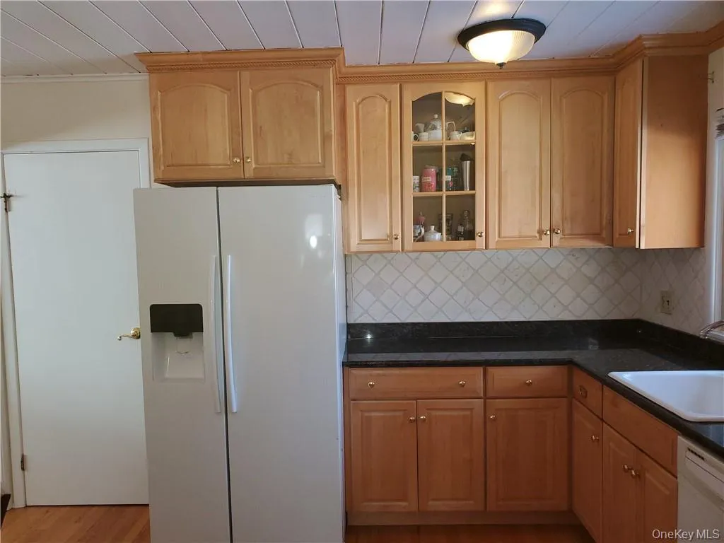 Kitchen featuring dark countertops, white appliances, glass insert cabinets, a sink, and backsplash Kitchen featuring dark countertops, white appliances, glass insert cabinets, a sink, and backsplash