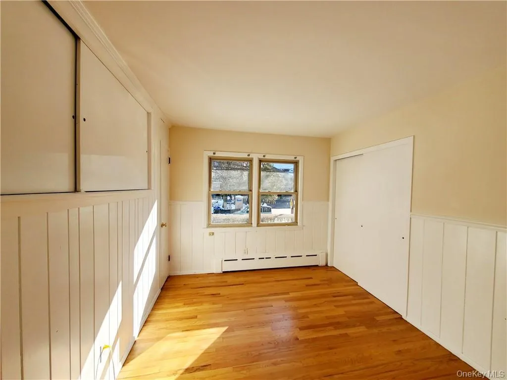 Empty room featuring light wood-style floors, a wainscoted wall, and a baseboard radiator Empty room featuring light wood-style floors, a wainscoted wall, and a baseboard radiator