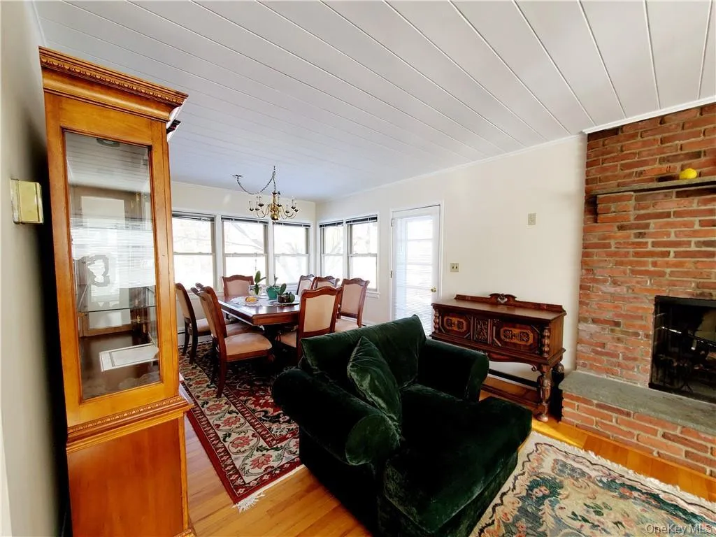 Living room featuring crown molding, light wood-style flooring, a brick fireplace, and a notable chandelier Living room featuring crown molding, light wood-style flooring, a brick fireplace, and a notable chandelier