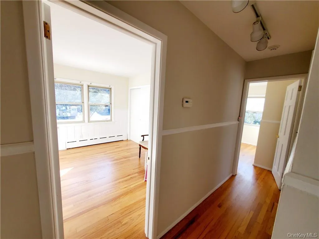 Corridor with a baseboard heating unit, track lighting, and light wood-type flooring Corridor with a baseboard heating unit, track lighting, and light wood-type flooring