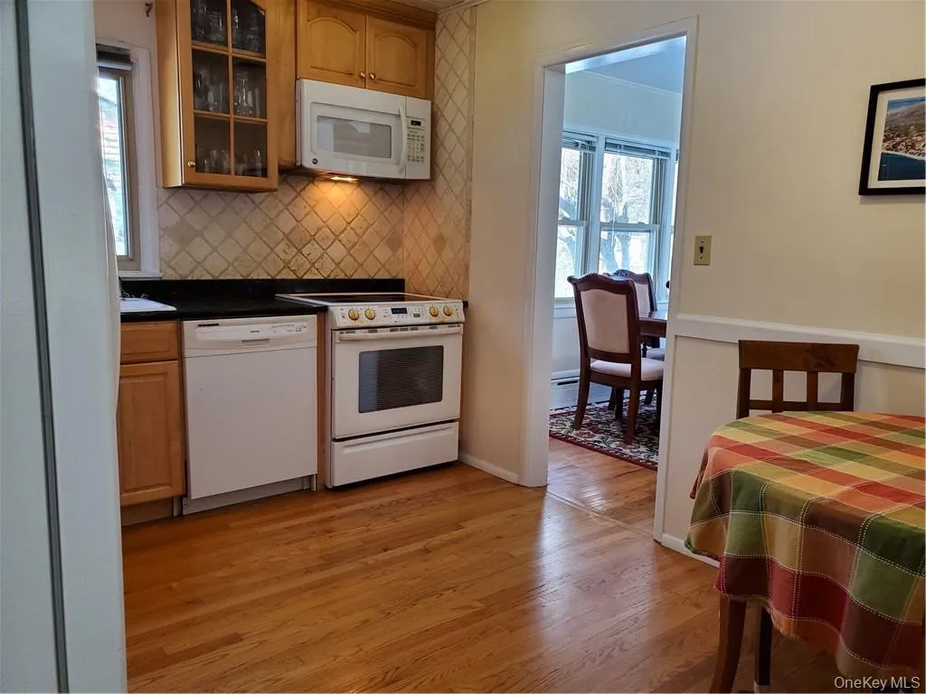 Kitchen featuring decorative backsplash, light wood-style flooring, white appliances, and glass insert cabinets Kitchen featuring decorative backsplash, light wood-style flooring, white appliances, and glass insert cabinets