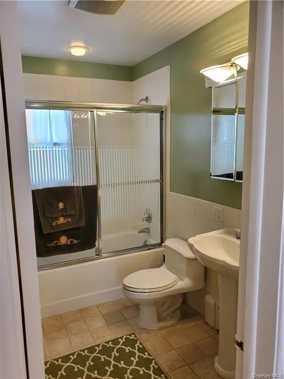 Bathroom featuring visible vents, tile walls, tile patterned floors, toilet, and enclosed tub / shower combo Bathroom featuring visible vents, tile walls, tile patterned floors, toilet, and enclosed tub / shower combo