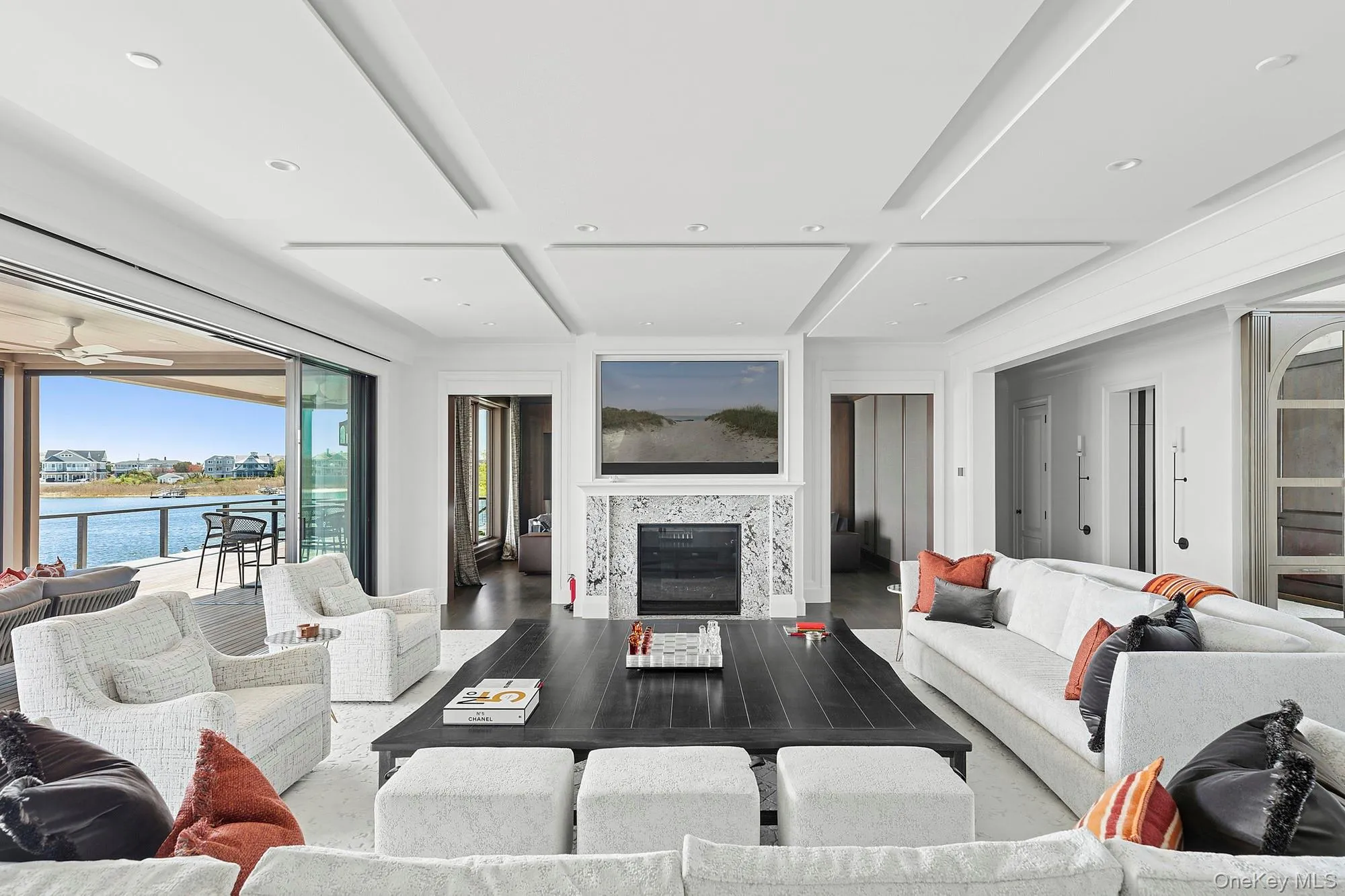 Living area featuring coffered ceiling, wood finished floors, a water view, a tiled fireplace, and beam ceiling Living area featuring coffered ceiling, wood finished floors, a water view, a tiled fireplace, and beam ceiling
