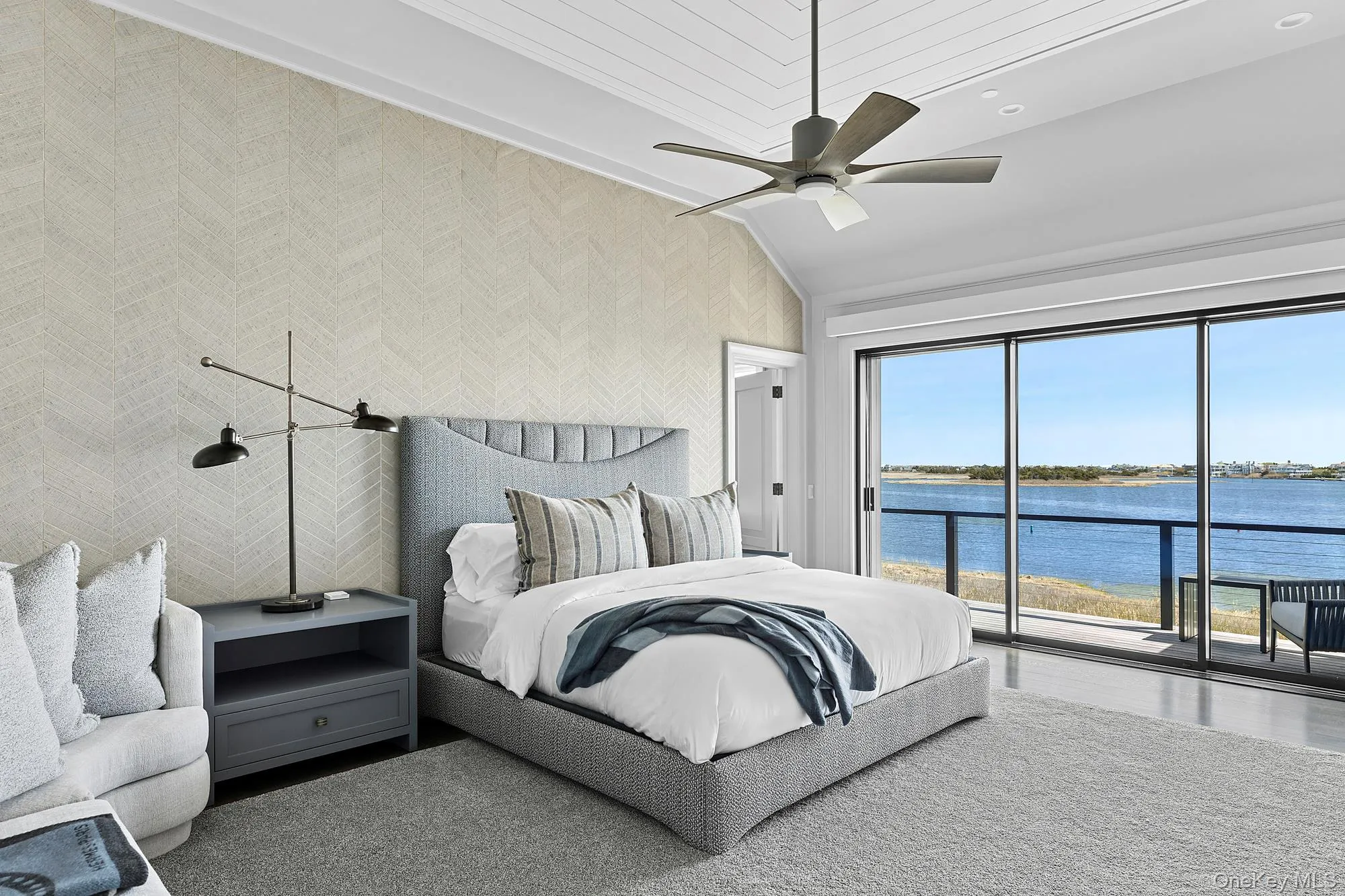 Bedroom featuring access to outside, a water view, vaulted ceiling, wallpapered walls, and a ceiling fan Bedroom featuring access to outside, a water view, vaulted ceiling, wallpapered walls, and a ceiling fan