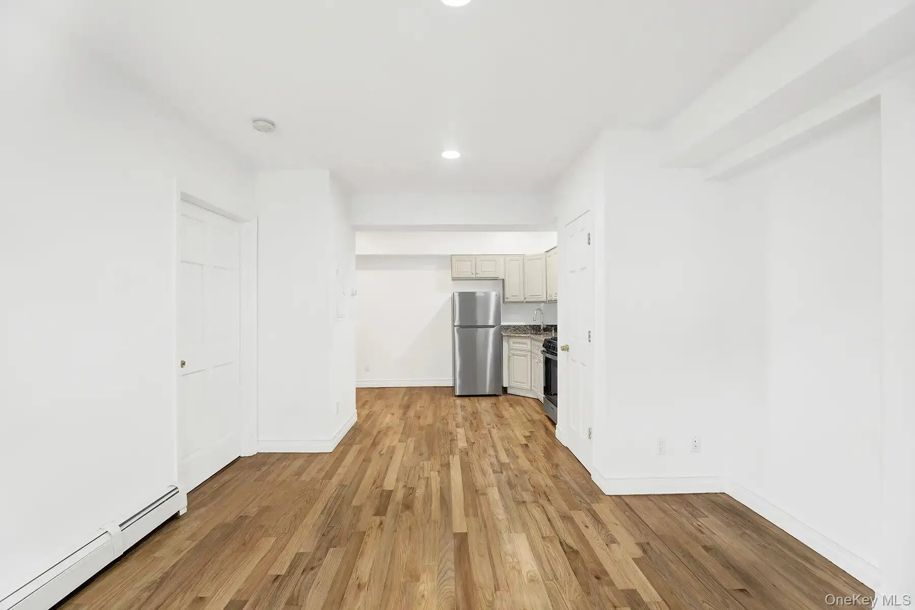 Unfurnished living room featuring light wood-type flooring, baseboard heating, and recessed lighting Unfurnished living room featuring light wood-type flooring, baseboard heating, and recessed lighting