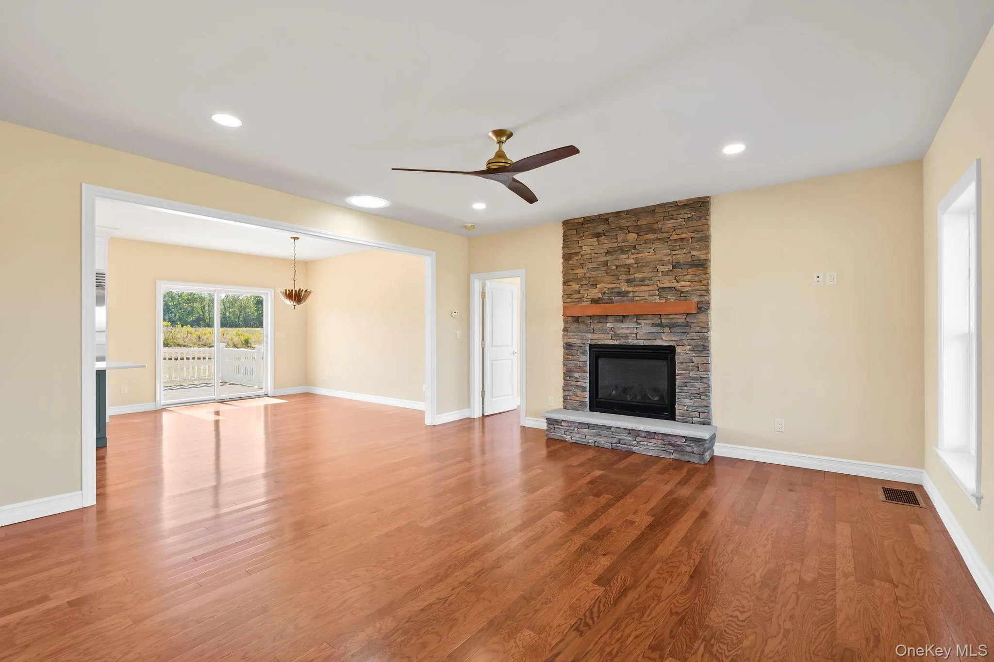 Unfurnished living room with a ceiling fan, wood finished floors, a stone fireplace, and recessed lighting Unfurnished living room with a ceiling fan, wood finished floors, a stone fireplace, and recessed lighting