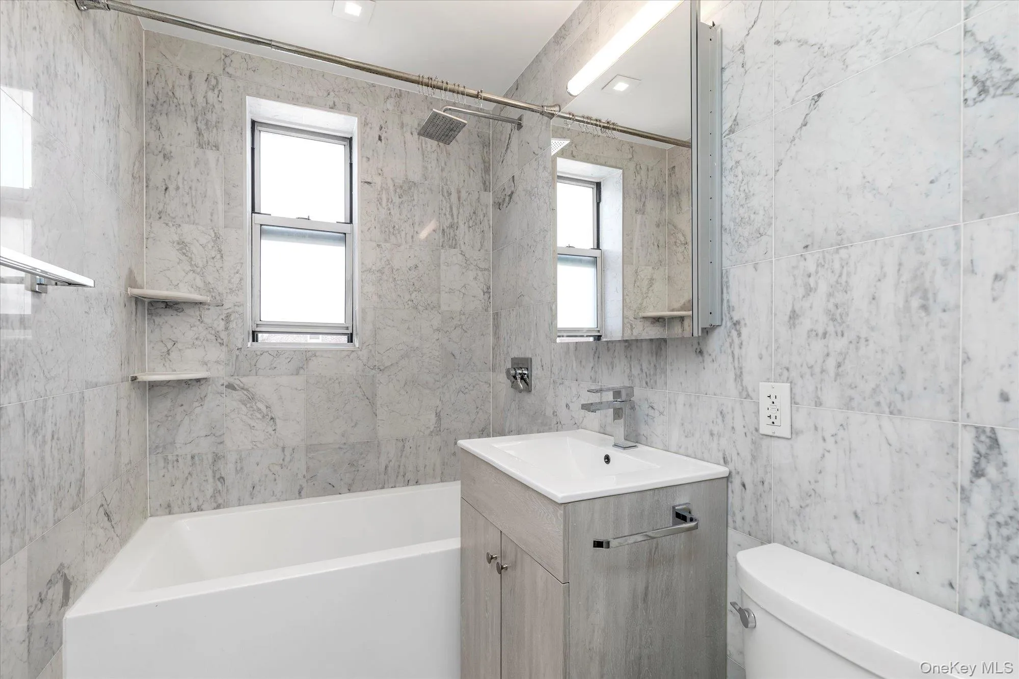 Bathroom featuring vanity, shower / bathtub combination, tile walls, and plenty of natural light Bathroom featuring vanity, shower / bathtub combination, tile walls, and plenty of natural light