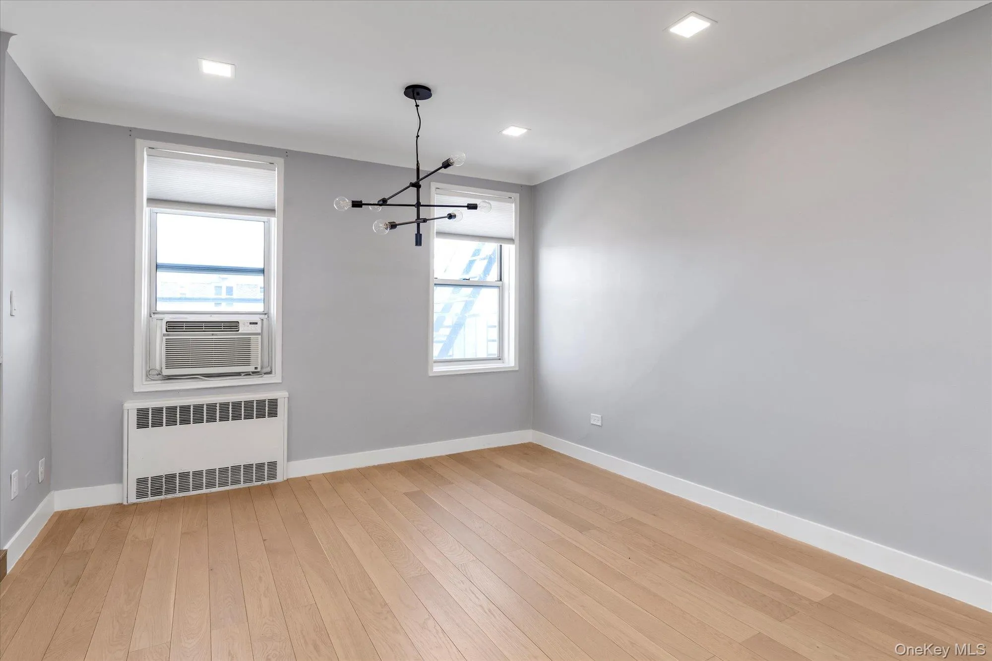 Unfurnished dining area with radiator, light wood-style flooring, hanging lights, cooling unit and recessed lighting Unfurnished dining area with radiator, light wood-style flooring, hanging lights, cooling unit and recessed lighting