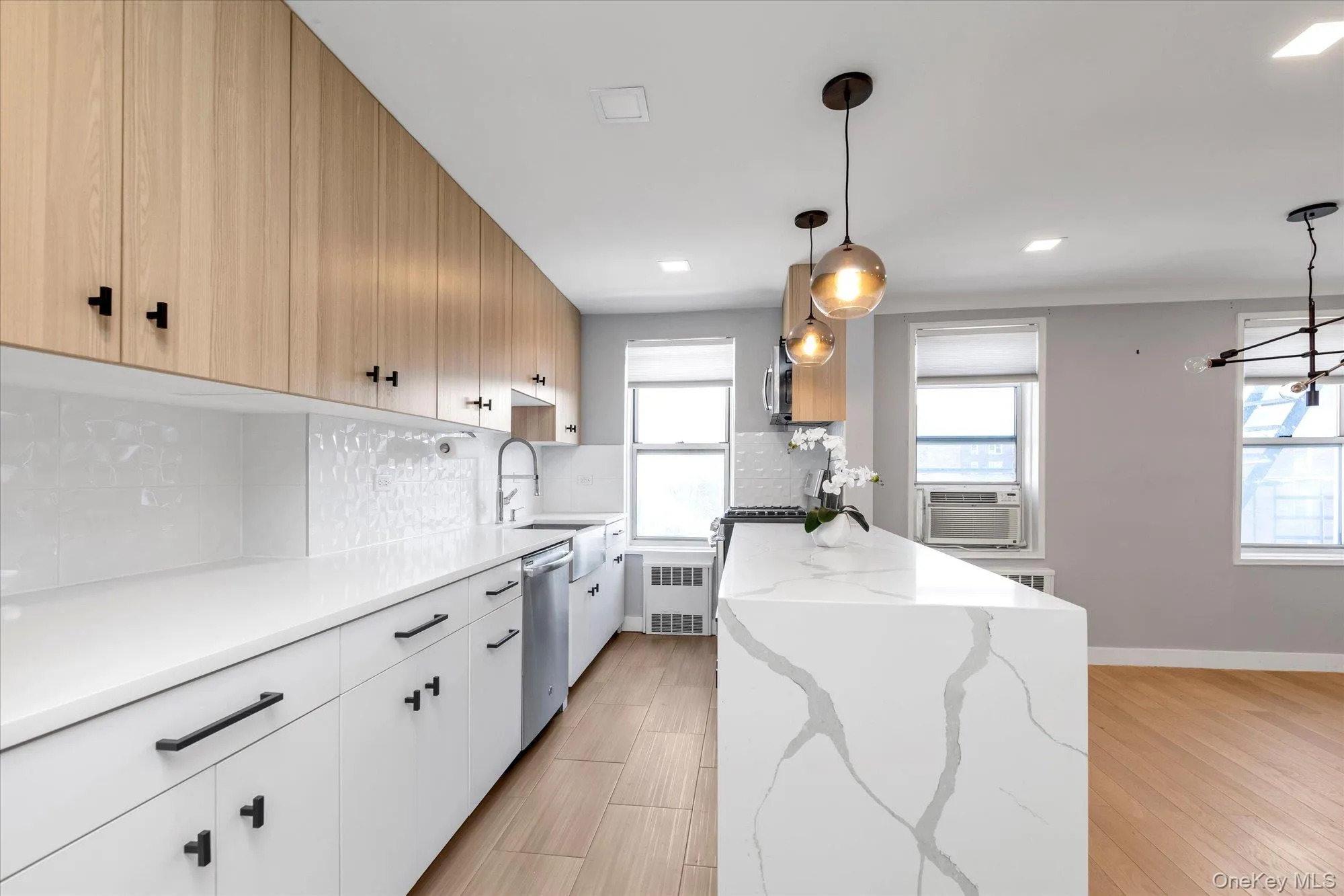 Kitchen featuring backsplash, light stone countertops, light wood-style flooring, stainless steel dishwasher, radiator heating unit, recessed lighting Kitchen featuring backsplash, light stone countertops, light wood-style flooring, stainless steel dishwasher, radiator heating unit, recessed lighting