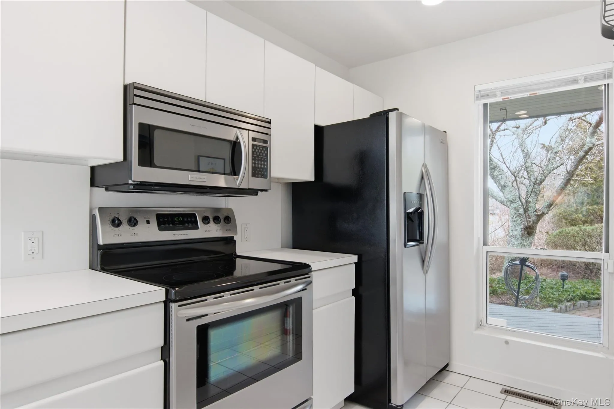 Kitchen with stainless steel appliances, light countertops, white cabinets, and light tile patterned floors Kitchen with stainless steel appliances, light countertops, white cabinets, and light tile patterned floors