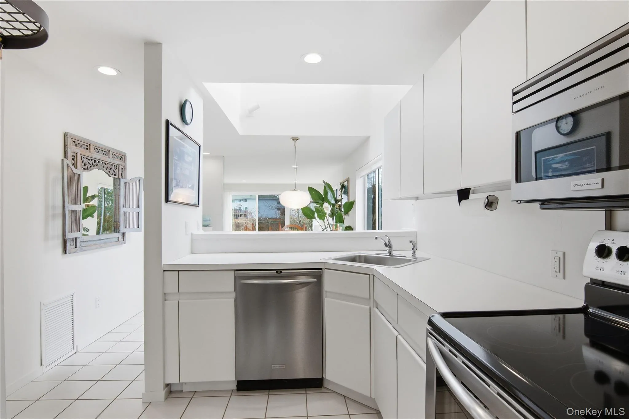 Kitchen featuring stainless steel appliances, white cabinets, light countertops, light tile patterned floors, and decorative light fixtures Kitchen featuring stainless steel appliances, white cabinets, light countertops, light tile patterned floors, and decorative light fixtures