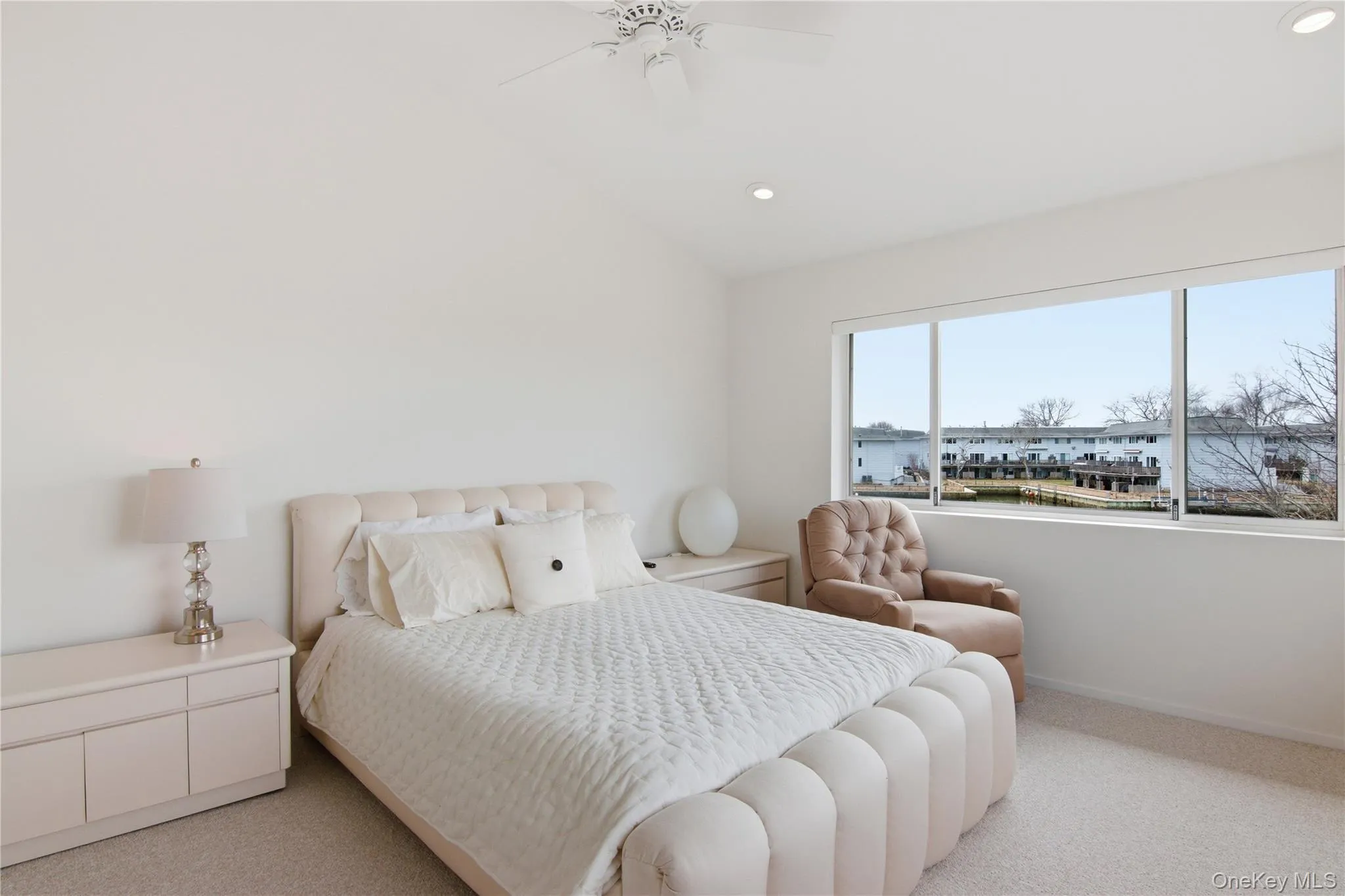 Bedroom featuring vaulted ceiling, light colored carpet, a ceiling fan, and recessed lighting with views of the village and water Bedroom featuring vaulted ceiling, light colored carpet, a ceiling fan, and recessed lighting with views of the village and water