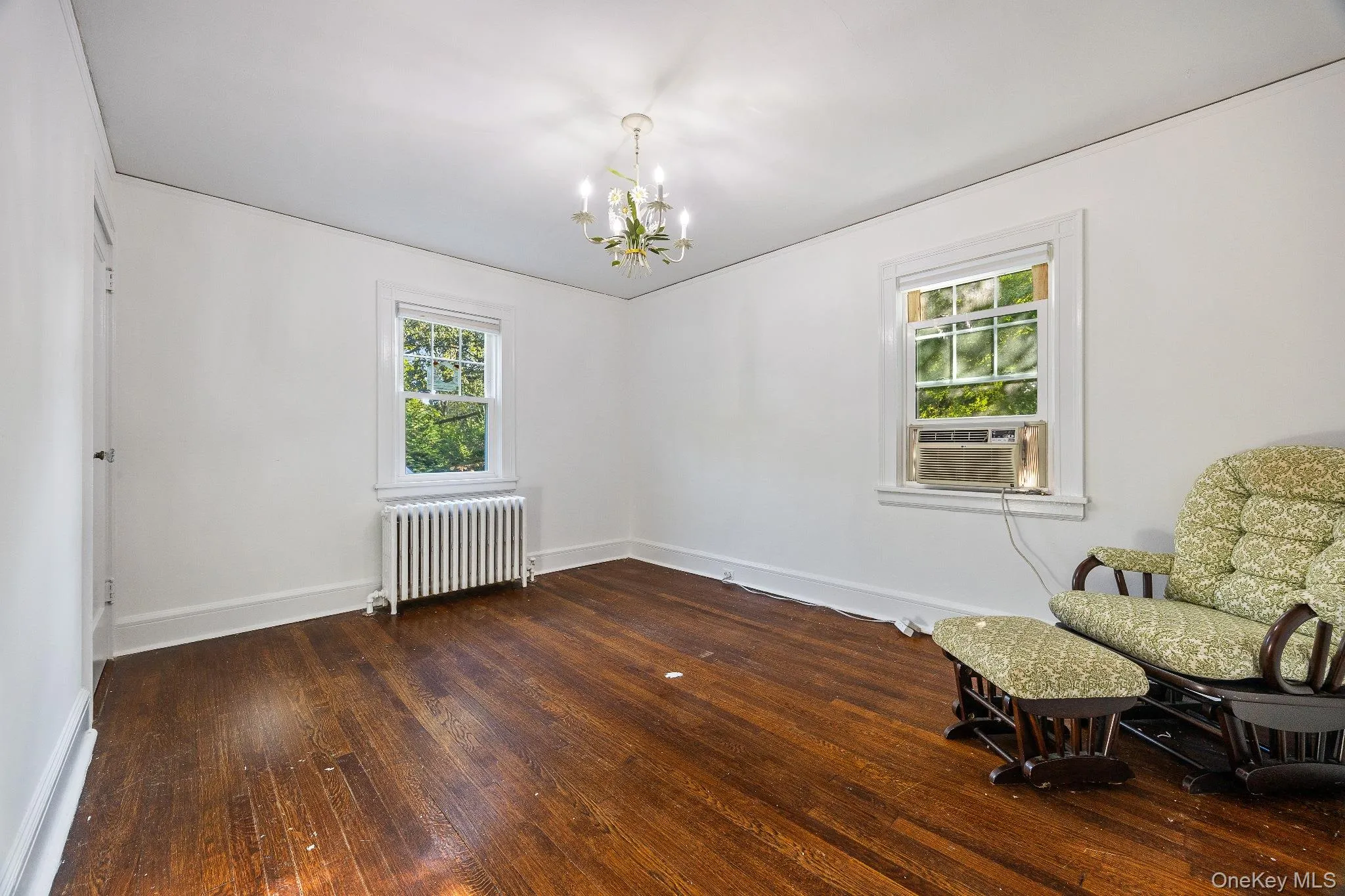 Unfurnished room featuring radiator heating unit, plenty of natural light, dark wood finished floors, and a chandelier Unfurnished room featuring radiator heating unit, plenty of natural light, dark wood finished floors, and a chandelier