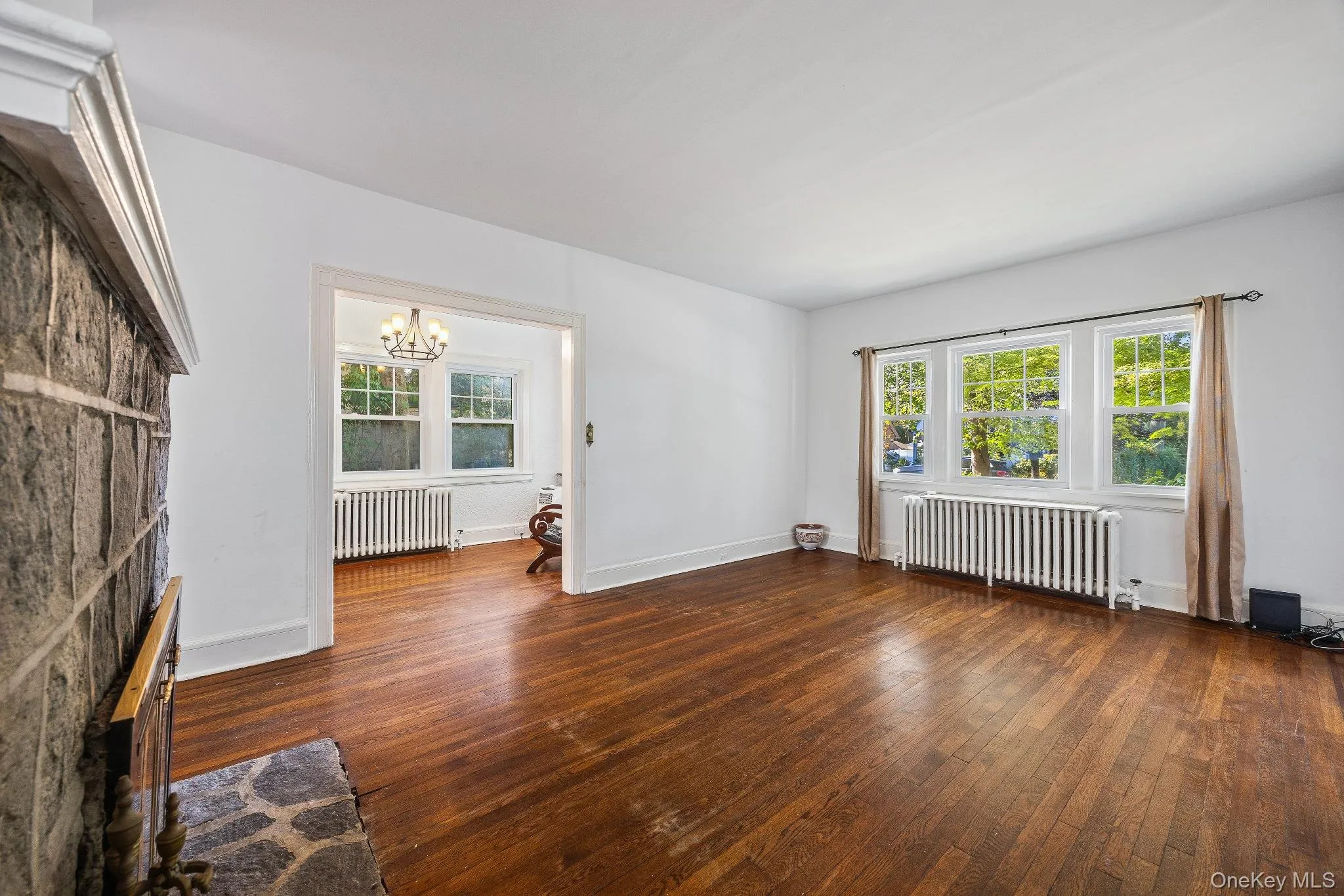 Unfurnished living room with radiator, dark wood-style floors, a chandelier, and plenty of natural light Unfurnished living room with radiator, dark wood-style floors, a chandelier, and plenty of natural light