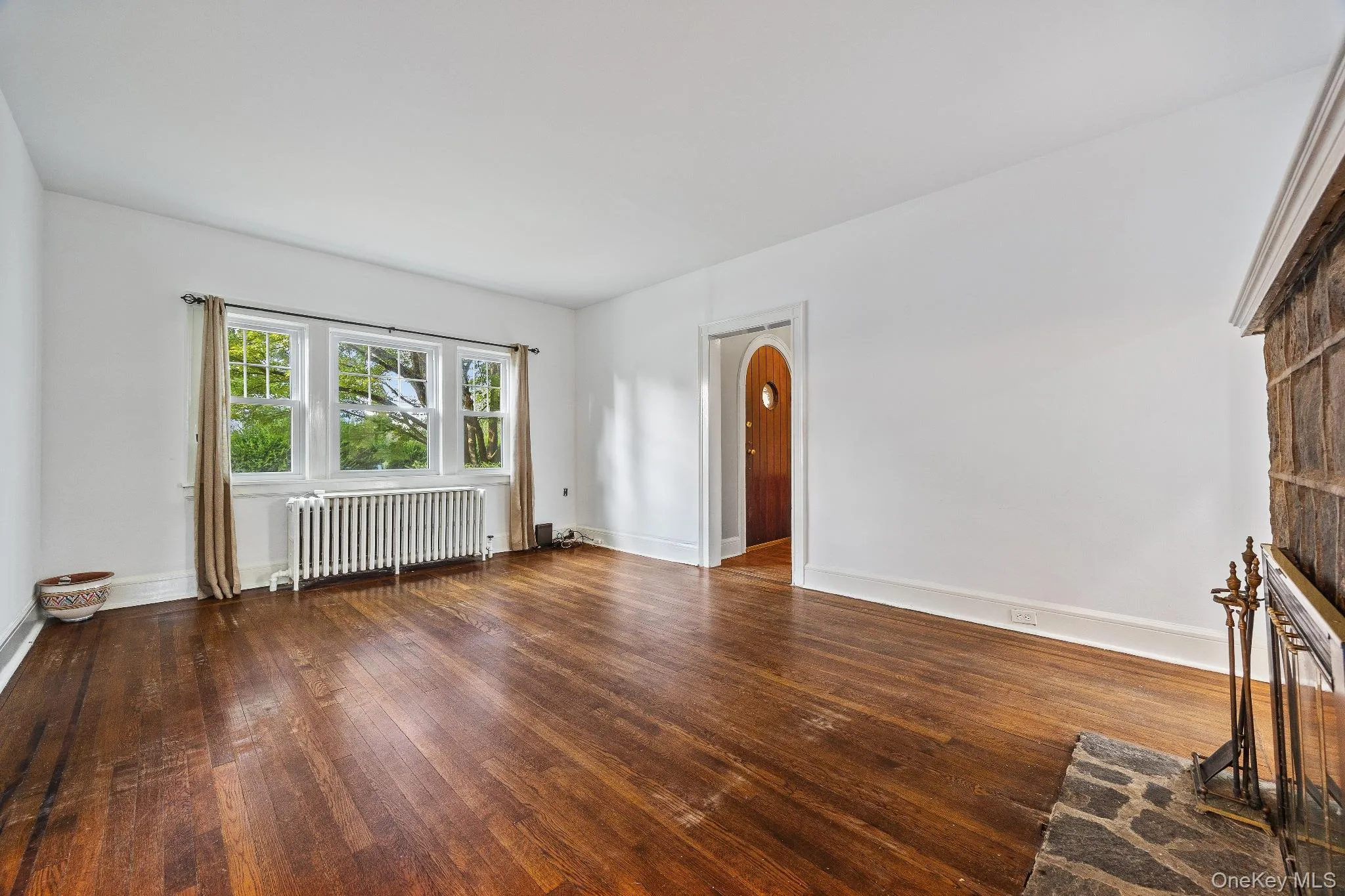 Unfurnished living room featuring radiator, hardwood / wood-style flooring, and arched walkways Unfurnished living room featuring radiator, hardwood / wood-style flooring, and arched walkways