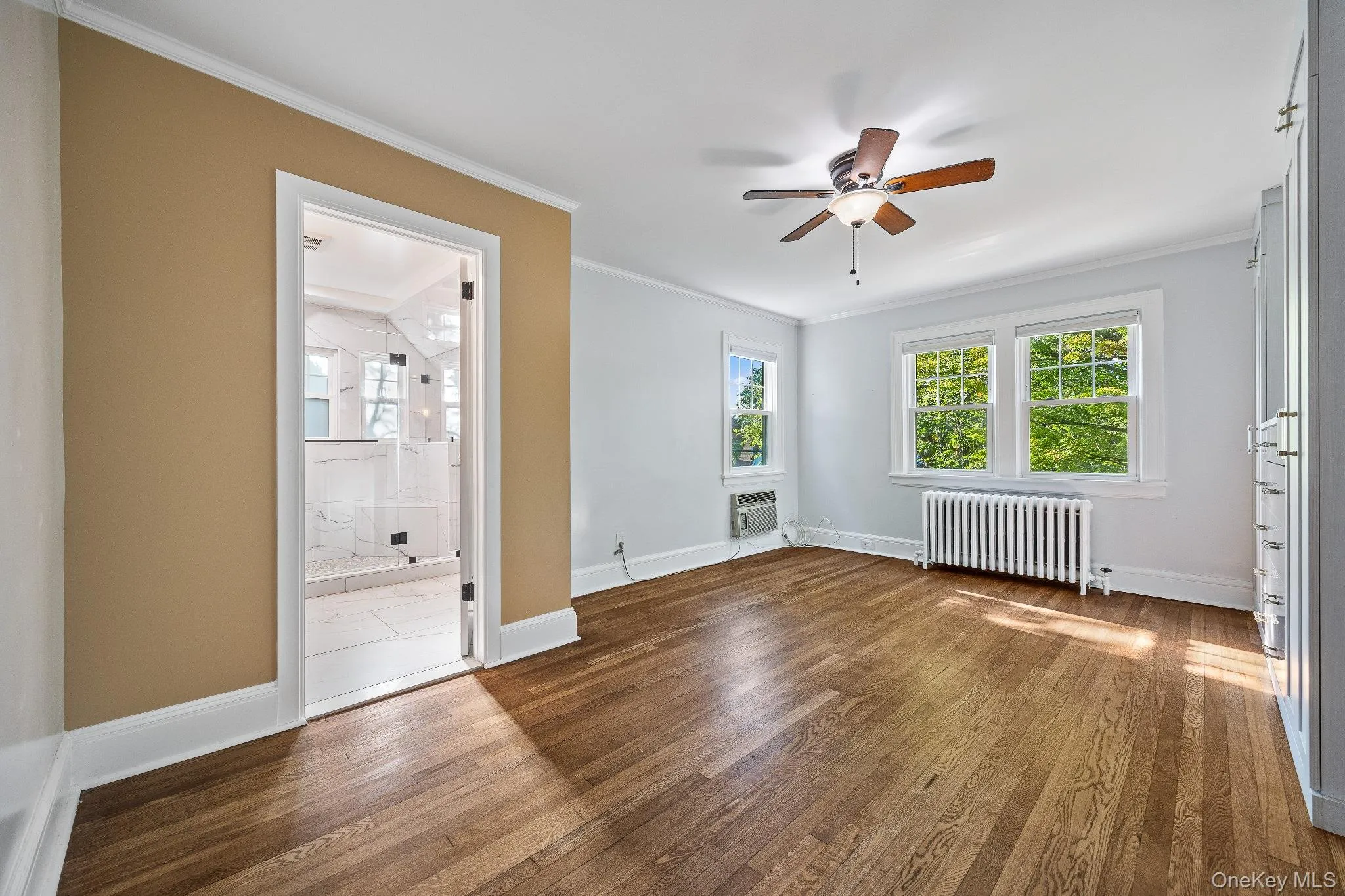 Unfurnished bedroom with ornamental molding, radiator heating unit, wood finished floors, and multiple windows Unfurnished bedroom with ornamental molding, radiator heating unit, wood finished floors, and multiple windows