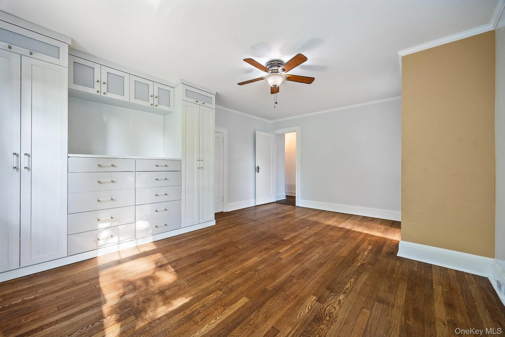 Unfurnished bedroom featuring crown molding, dark wood-style flooring, and a ceiling fan Unfurnished bedroom featuring crown molding, dark wood-style flooring, and a ceiling fan