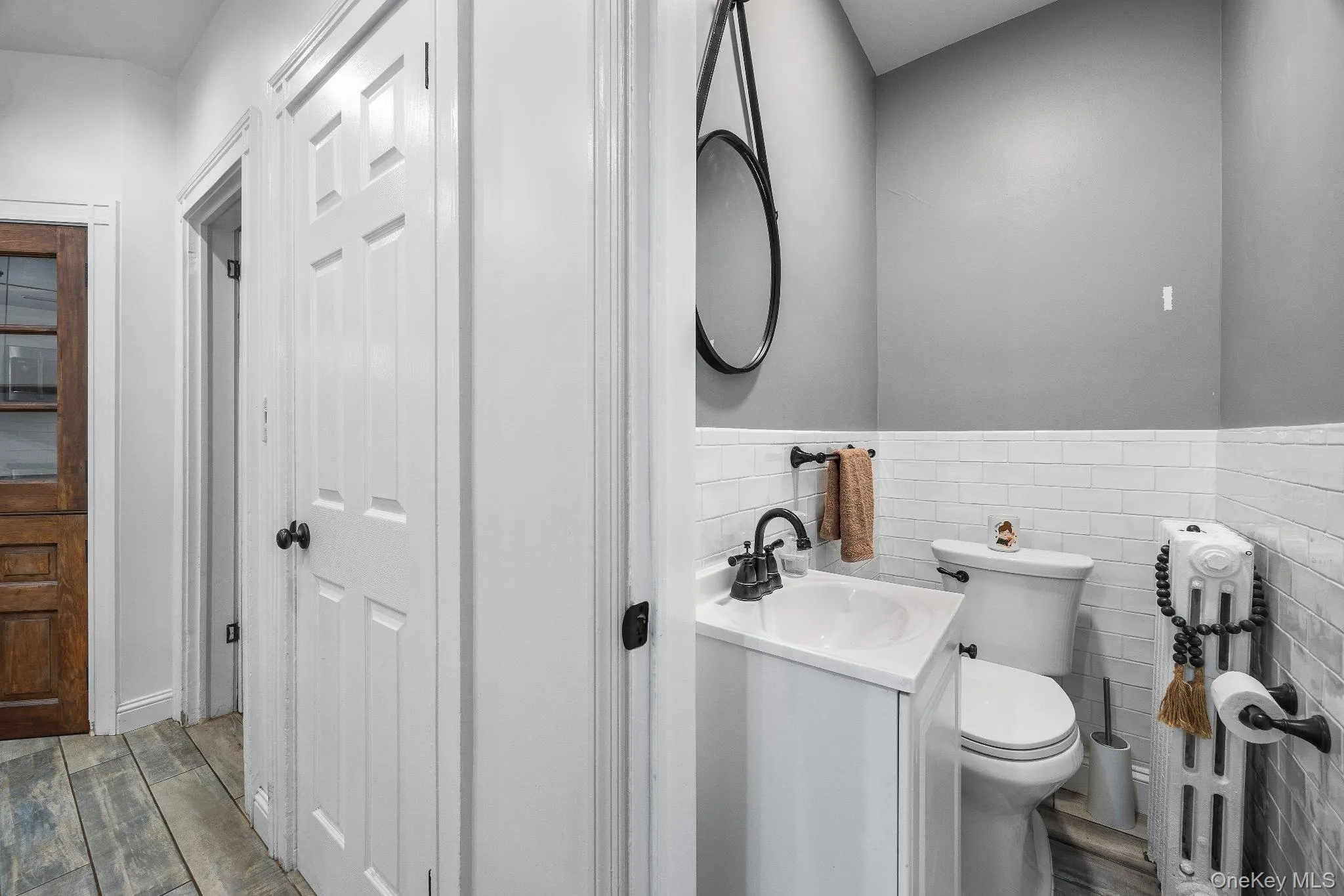 Bathroom featuring vanity, tile walls, wood finished floors, wainscoting, and radiator heating unit Bathroom featuring vanity, tile walls, wood finished floors, wainscoting, and radiator heating unit