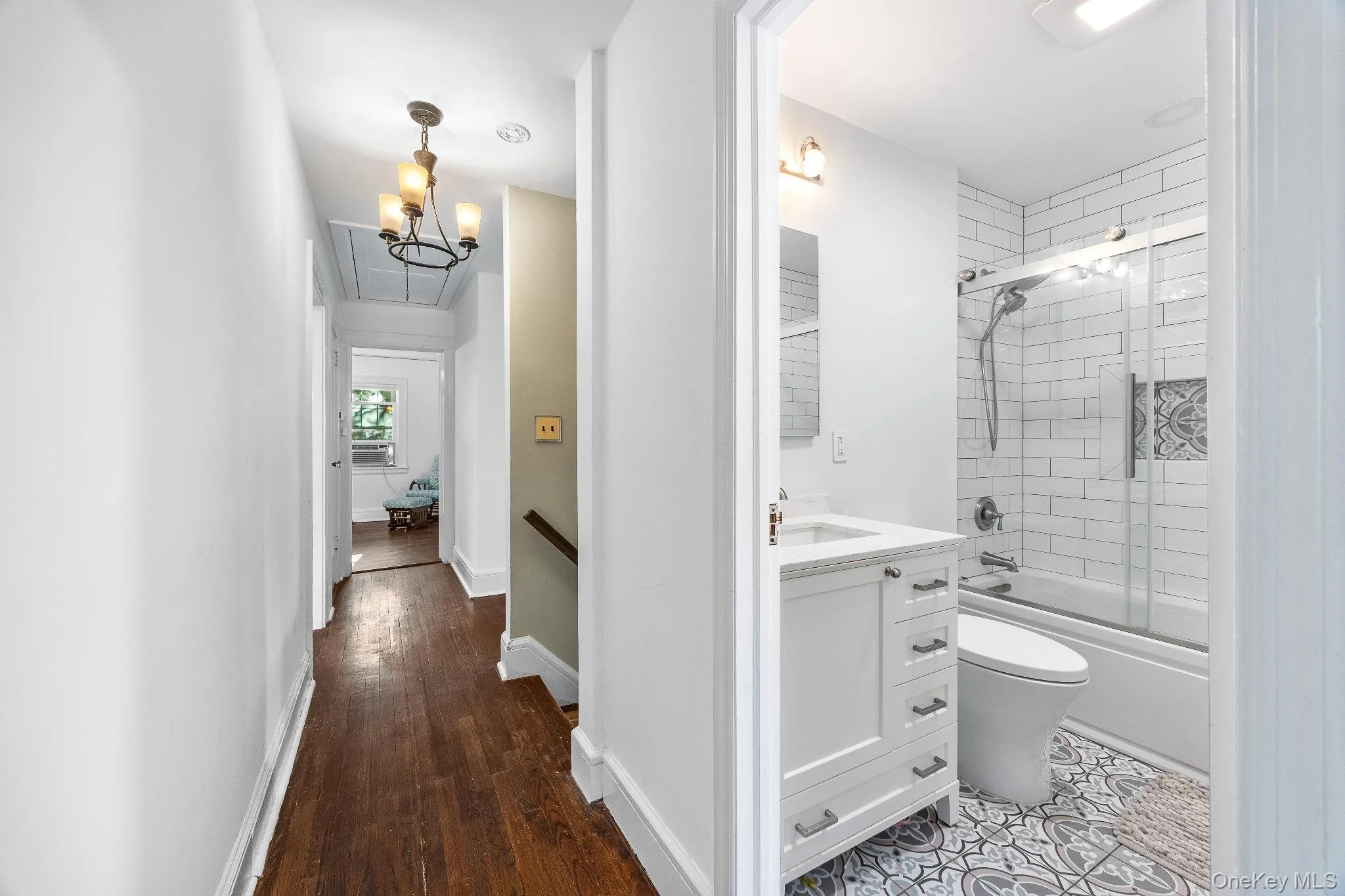 Full bathroom featuring shower / bath combination with glass door, vanity, dark wood-style floors, and a chandelier Full bathroom featuring shower / bath combination with glass door, vanity, dark wood-style floors, and a chandelier