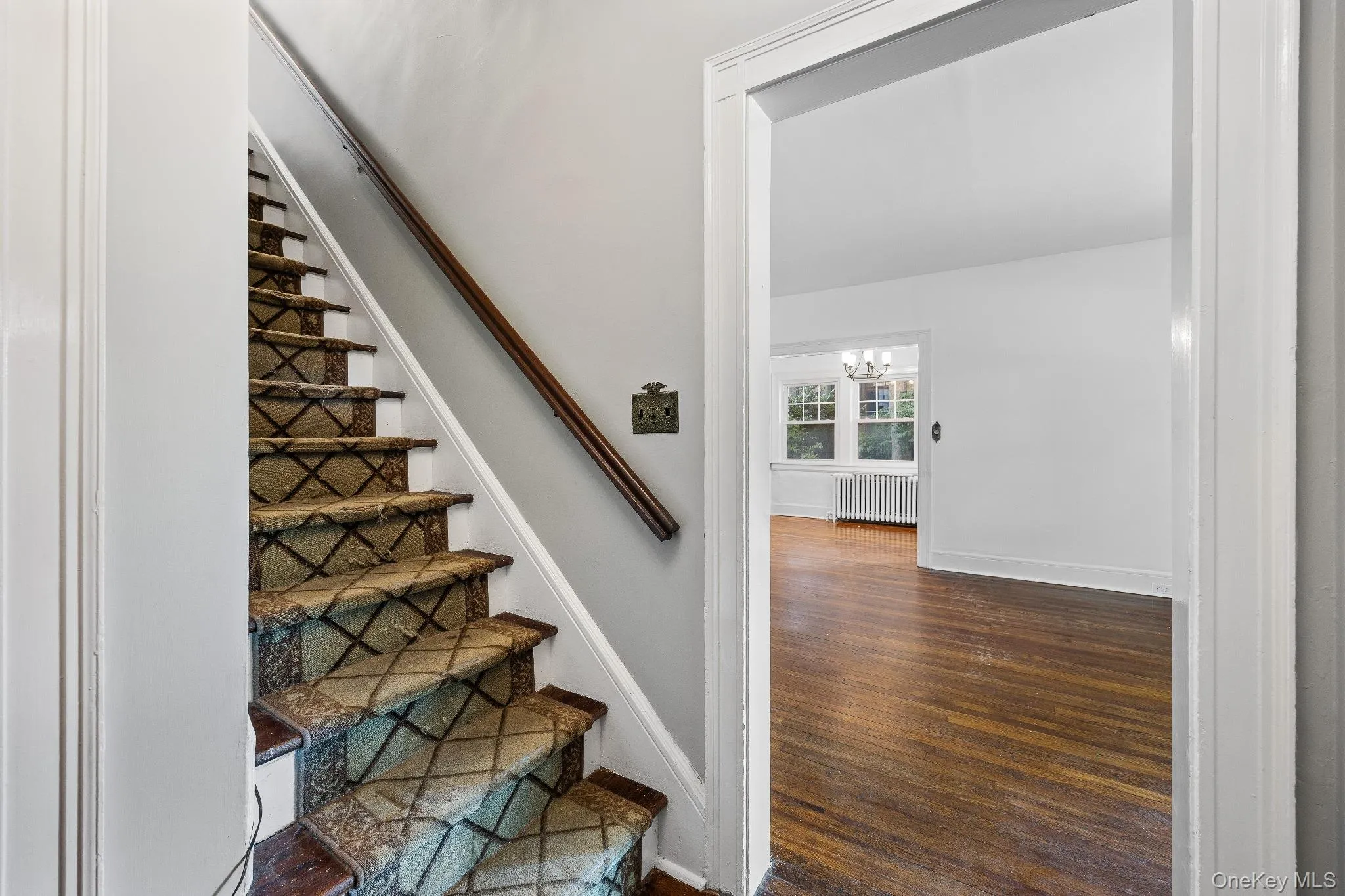 Staircase with wood finished floors, a chandelier, and radiator heating unit Staircase with wood finished floors, a chandelier, and radiator heating unit